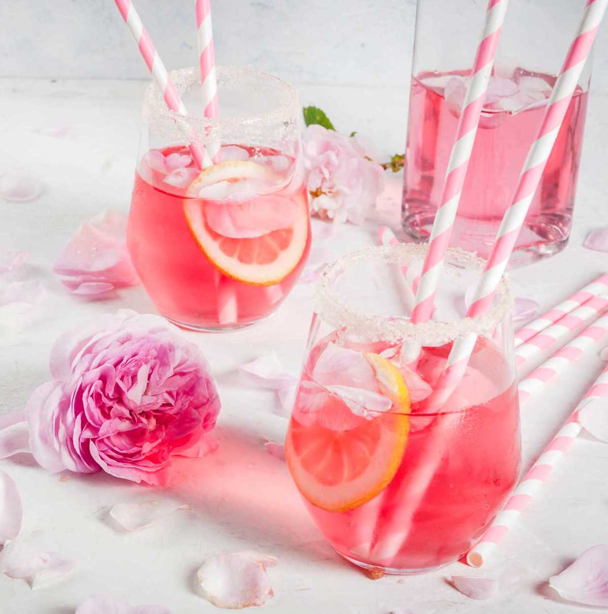 Two glasses of pink lemonade, a signature cocktail idea, surrounded by roses.