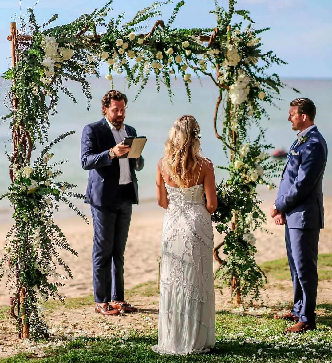 A bride and groom exchange vows under a beach wedding arch officiated by a wedding celebrant.
