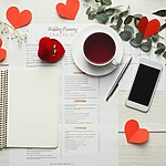 A notebook with red hearts and a cell phone placed on a white table.