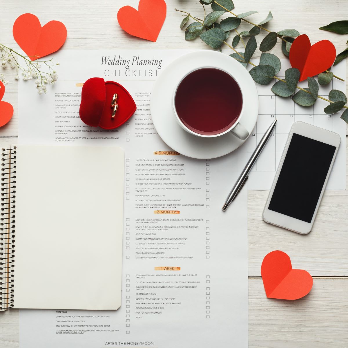 A notebook with red hearts and a cell phone placed on a white table.