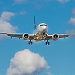 Wondering when is the best time to book a flight? A plane soars through a blue sky dotted with fluffy white clouds.