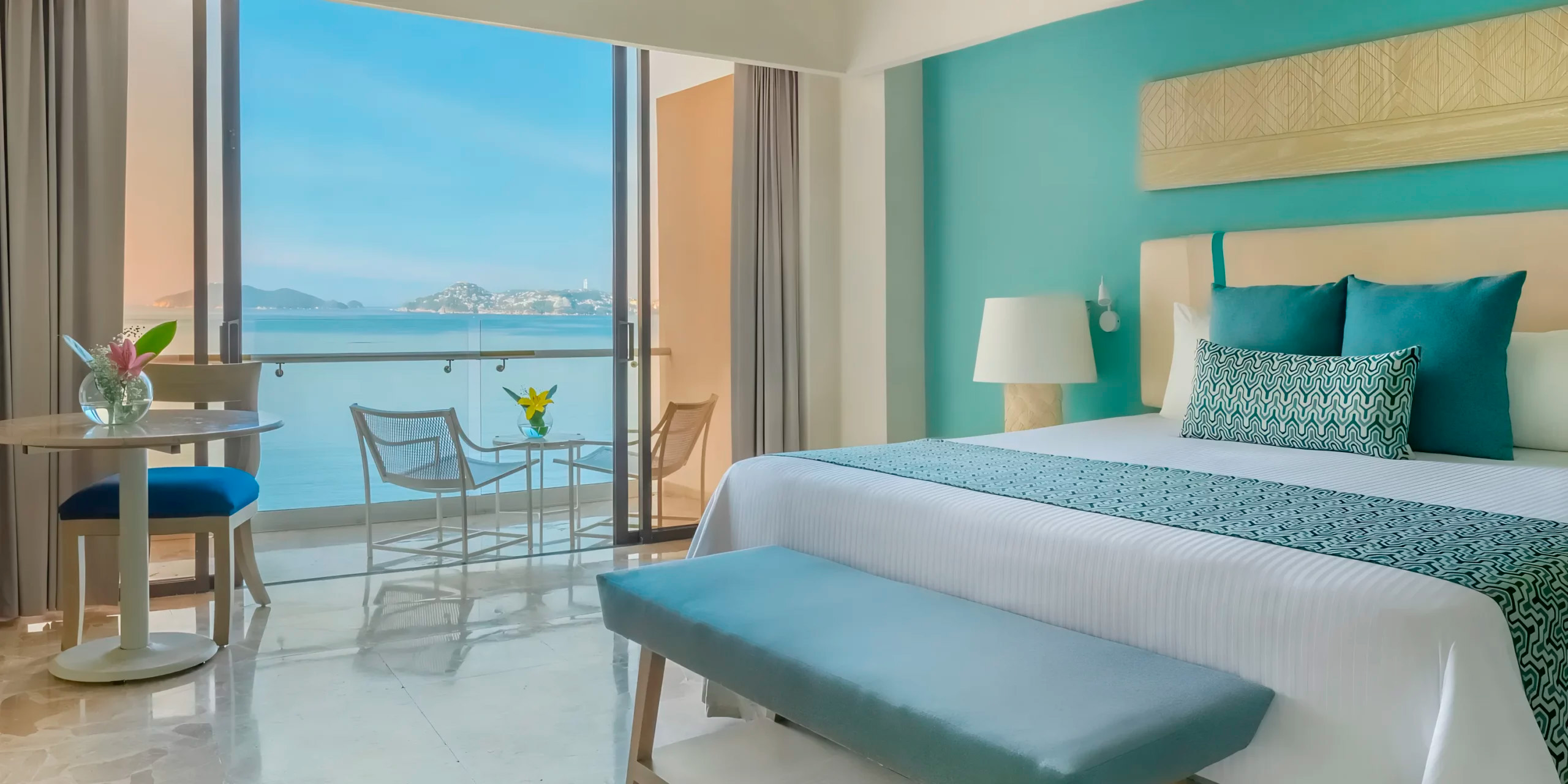 Dreams Acapulco: This ocean-view room features a cozy bed, chair, table, and open balcony doors—a perfect setting for your destination wedding getaway.