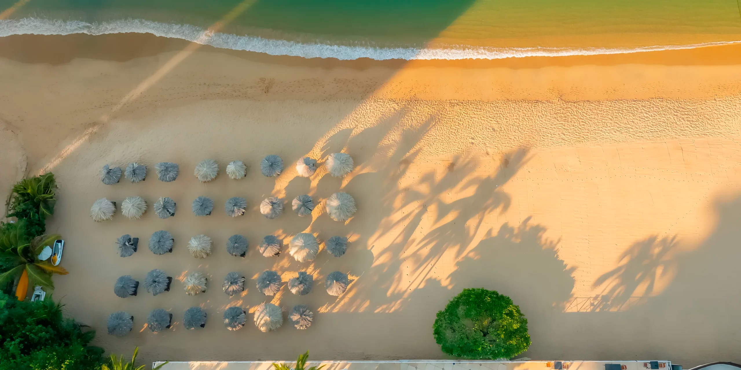 A stunning aerial view of Dreams Acapulco Resort showcases its picturesque beach, adorned with umbrellas casting palm shadows and waves gently meeting the shore—a perfect setting for a destination wedding.