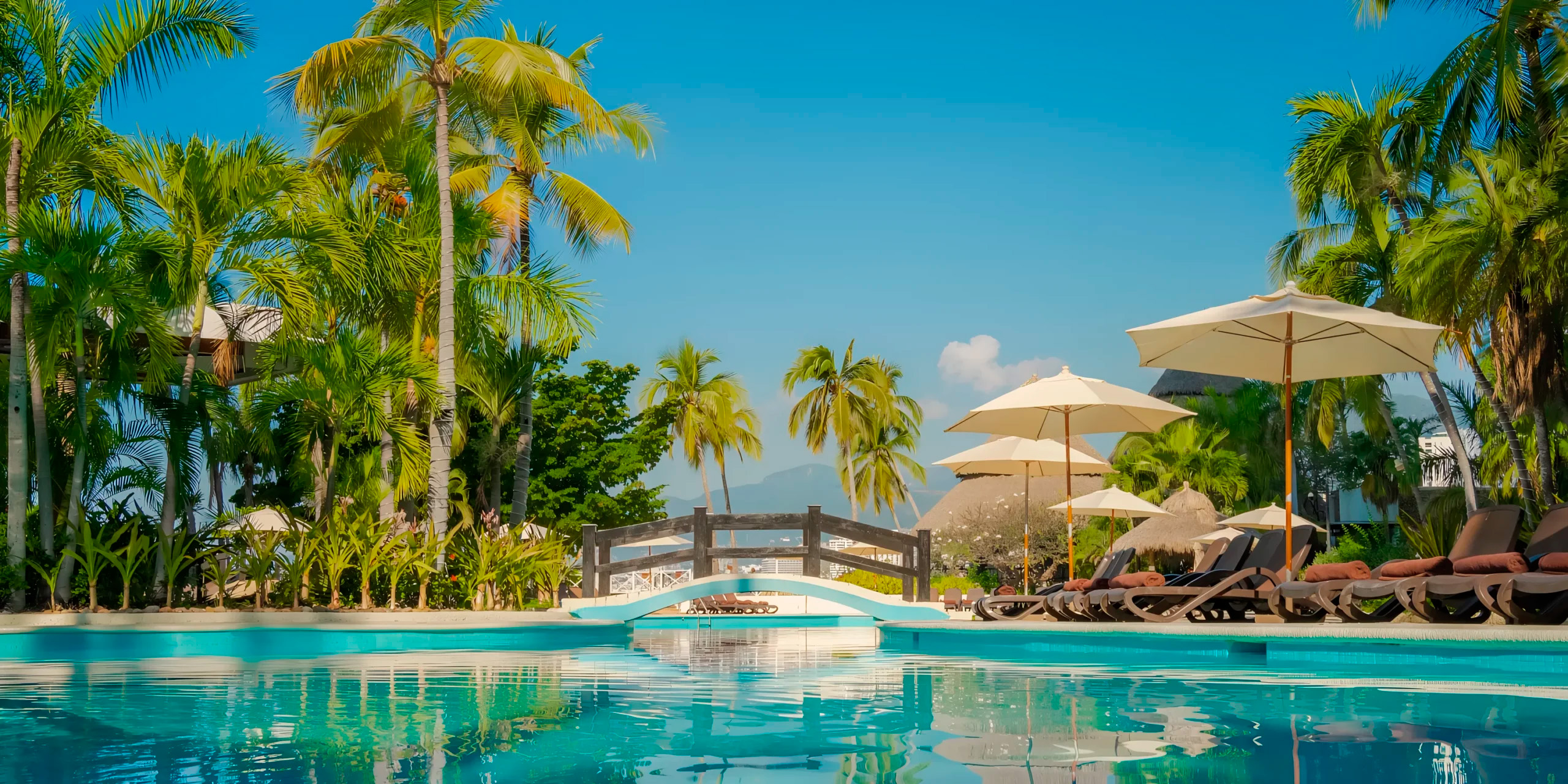 Dreams Acapulco Resort & Spa is a perfect destination wedding venue, offering a picturesque poolside view complete with palm trees, sun loungers, and umbrellas.