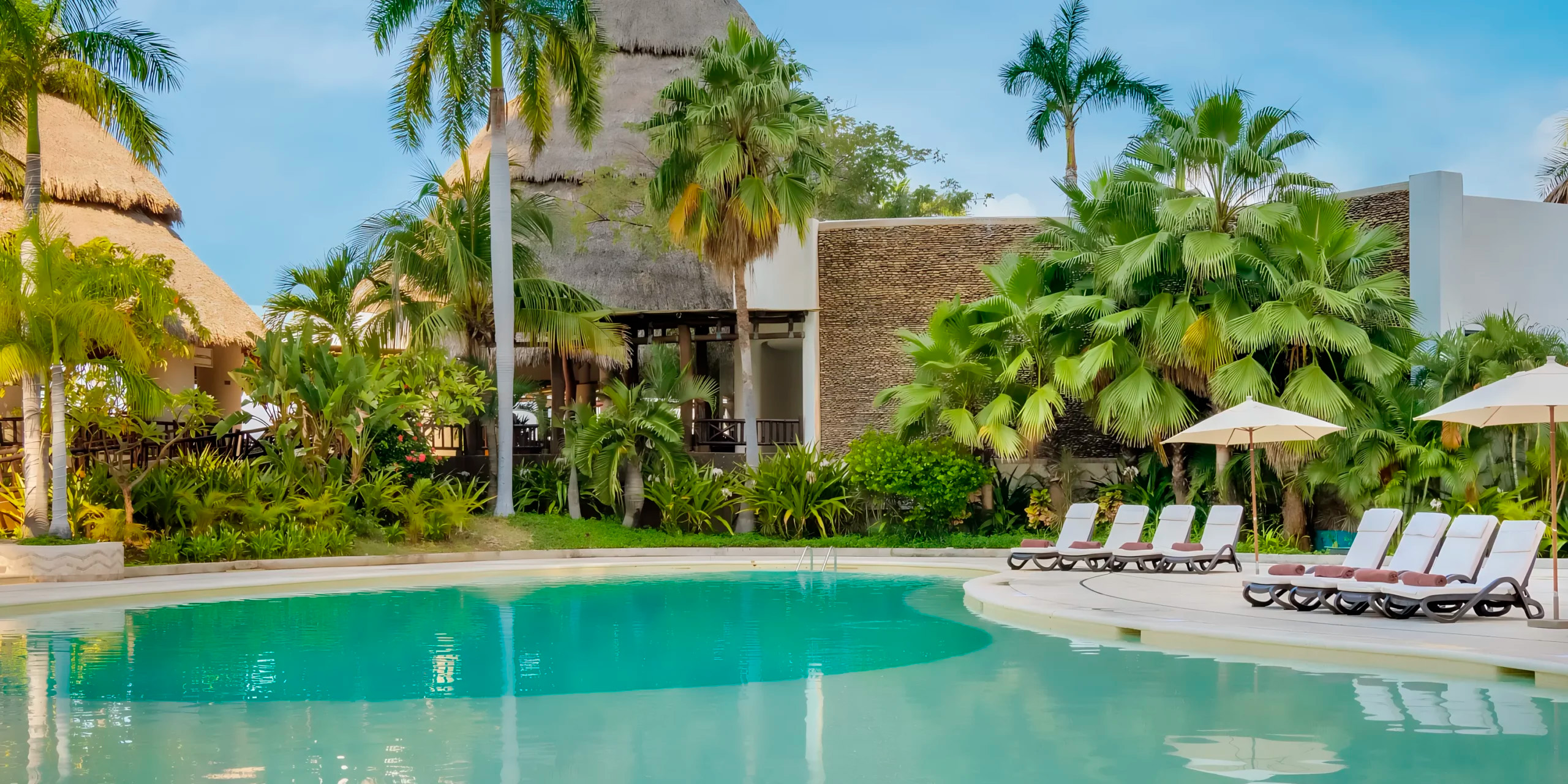 Dreams Acapulco Resort & Spa: An idyllic setting for a destination wedding, featuring a pool with lounge chairs, surrounded by palm trees and set against the backdrop of clear skies.