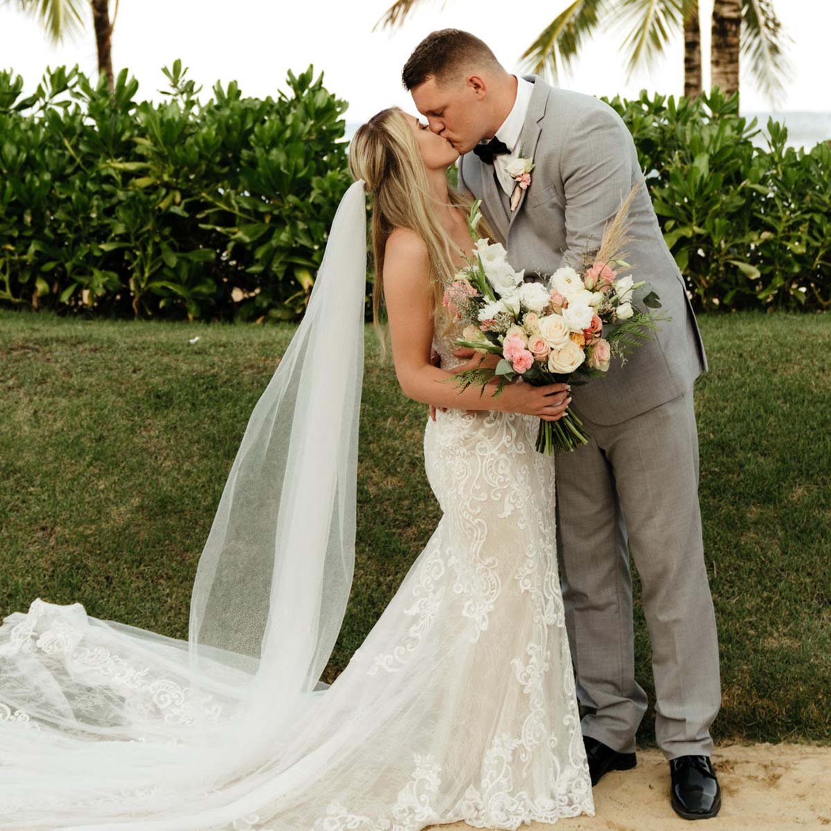 Makayla and Thomas kiss in front of palm trees.