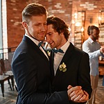 Two men in suits dancing to wedding music at a reception.