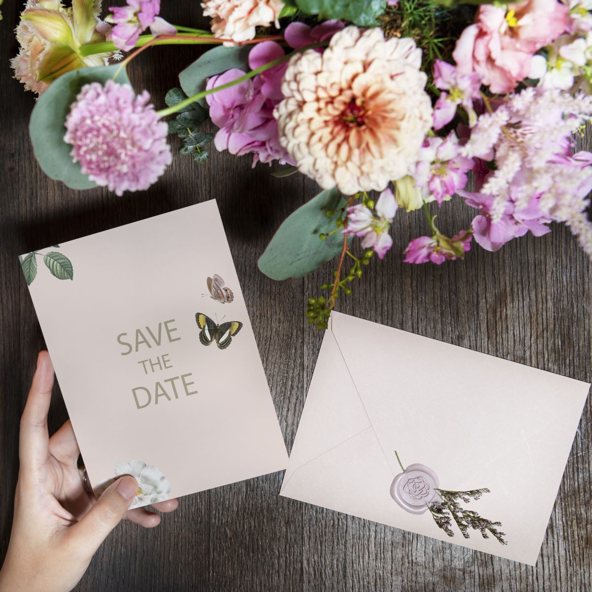 A hand holding a save the date card and flowers on a rustic wooden table for a destination wedding.