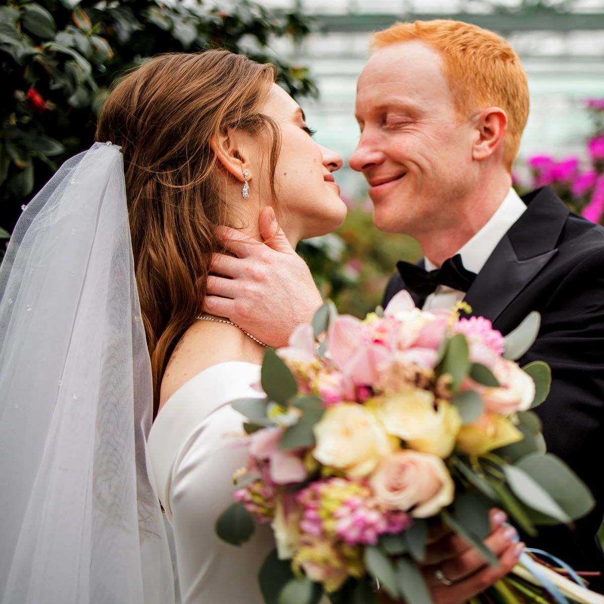 A bride and groom hugging in a greenhouse for their wedding poses.