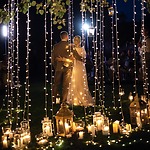 A bride and groom standing under a string of outdoor wedding lighting.