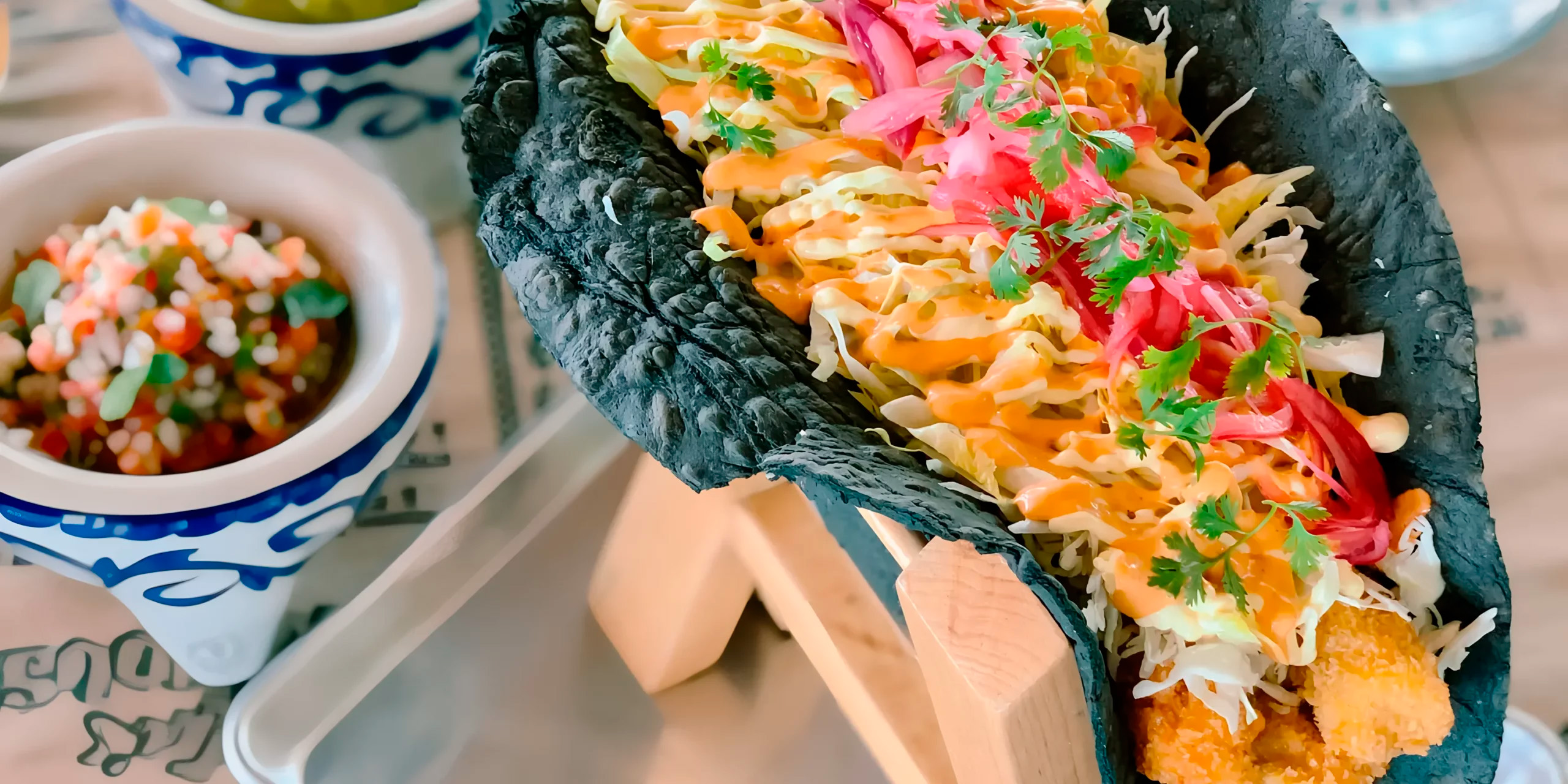 A vibrant taco nestled in a black shell, garnished to perfection and paired with a flavorful sauce, creates a delightful culinary experience at Margaritaville Island Reserve Riviera Maya, the perfect setting for a destination wedding.