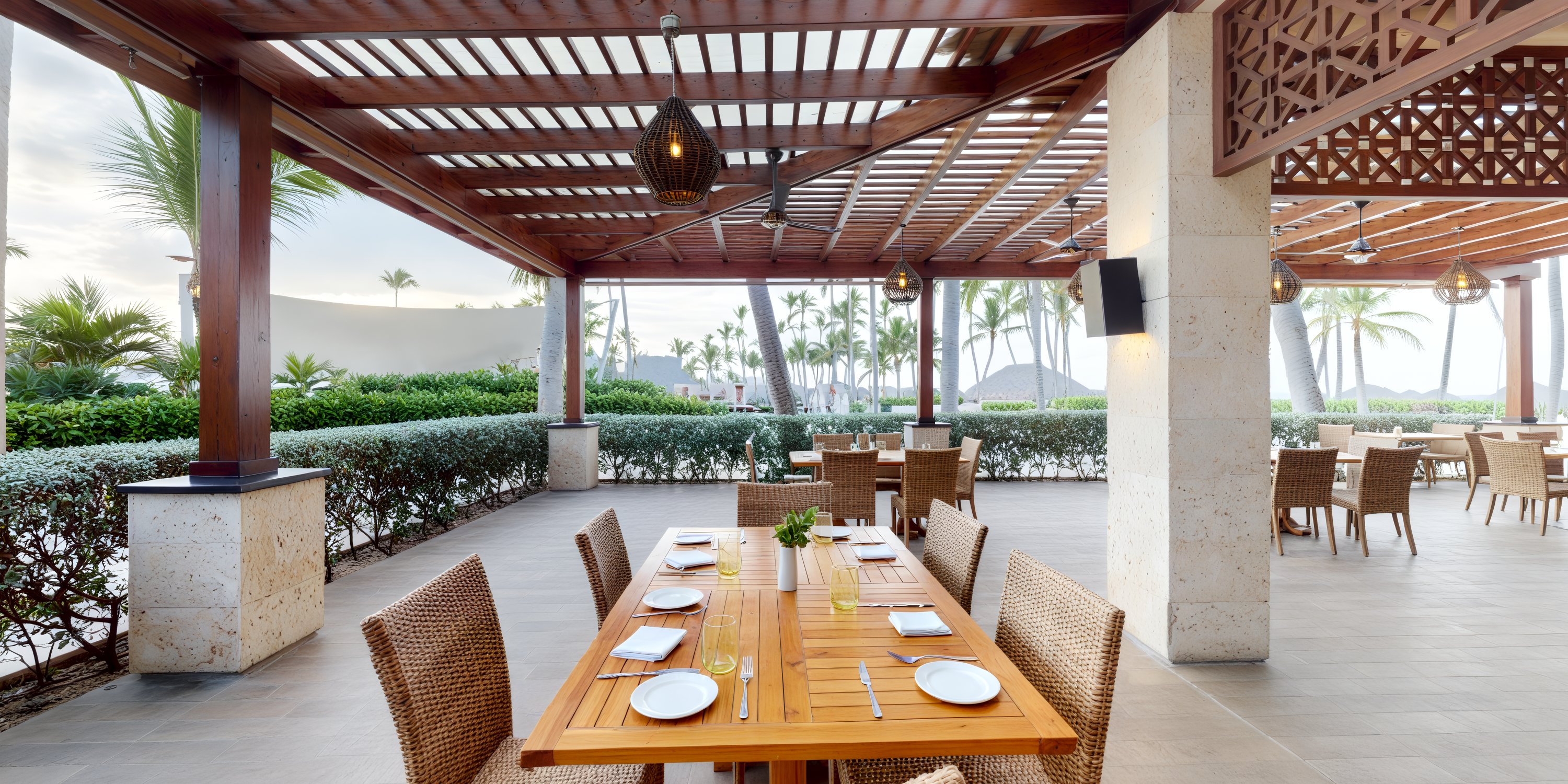 An outdoor dining area, perfect for a destination wedding, features a wooden table set for four and surrounded by elegant wicker chairs.