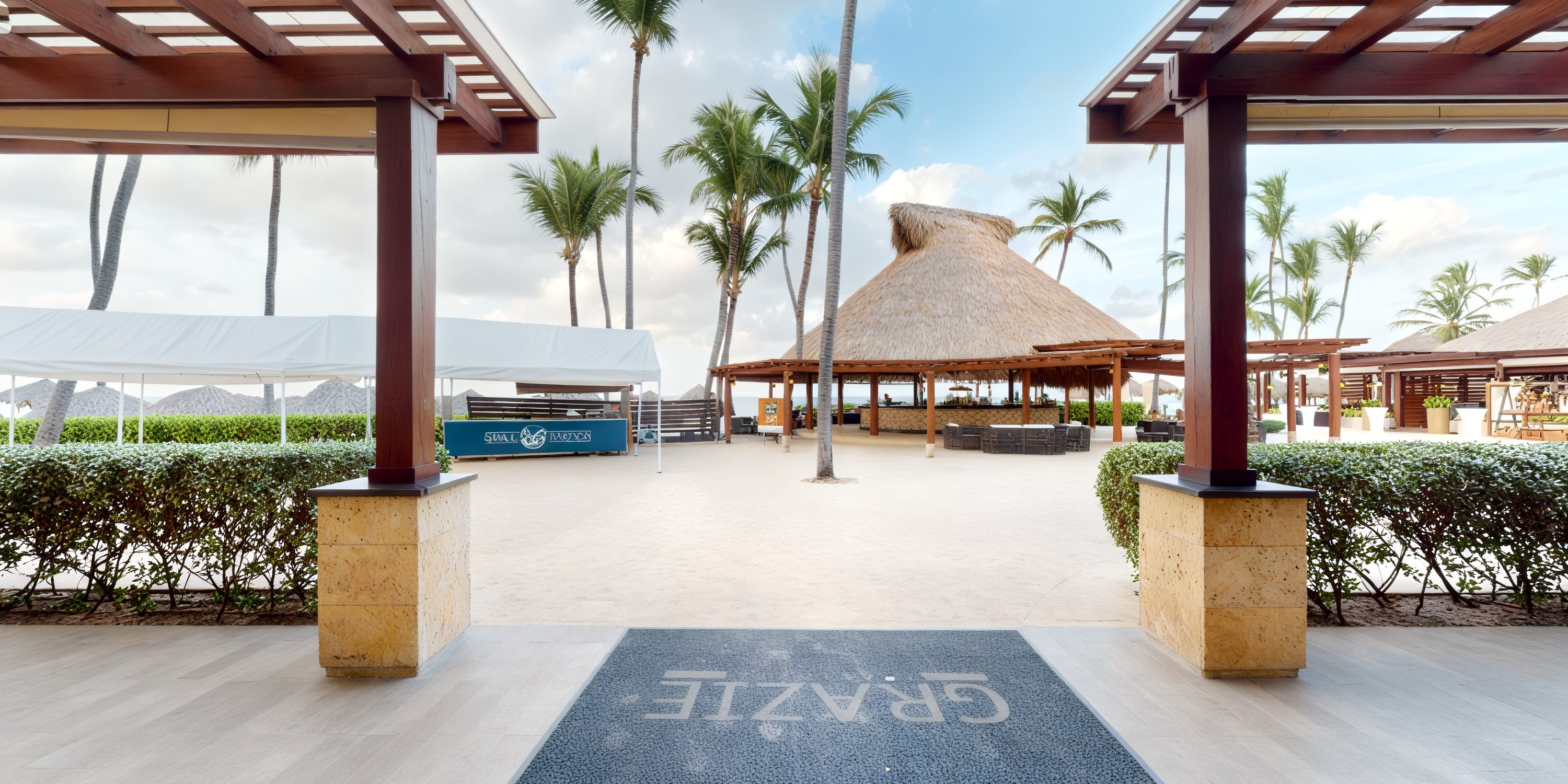A picturesque entrance view of a beachside resort, perfect for a destination wedding, featuring swaying palm trees and a charming thatched-roof hut.