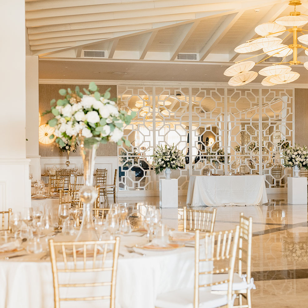 Elegant wedding reception hall decorated with white flowers, gold chairs, and geometric wall designs.