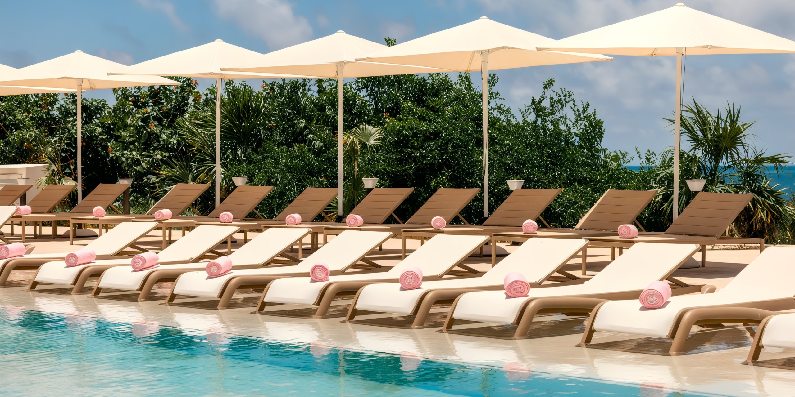 Rows of empty poolside lounge chairs with rolled towels under white umbrellas, set by a clear swimming pool surrounded by lush greenery at AVA Resort Cancun.