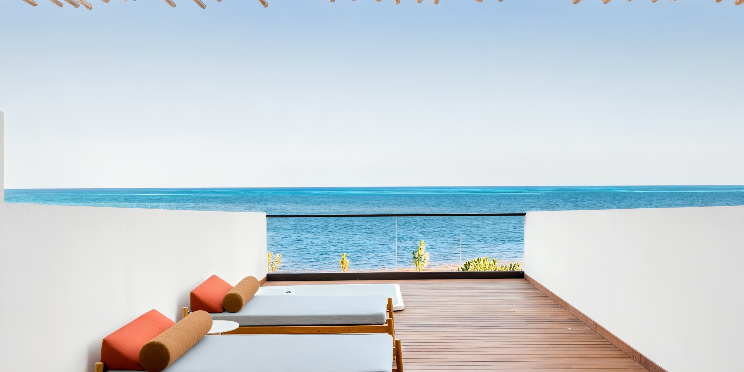 Two sun loungers with orange cushions enhance the wooden deck at AVA Resort Cancun, providing a stunning view of the clear blue ocean under a cloudless sky, with a glass railing elegantly dividing the deck from the breathtaking scenery.