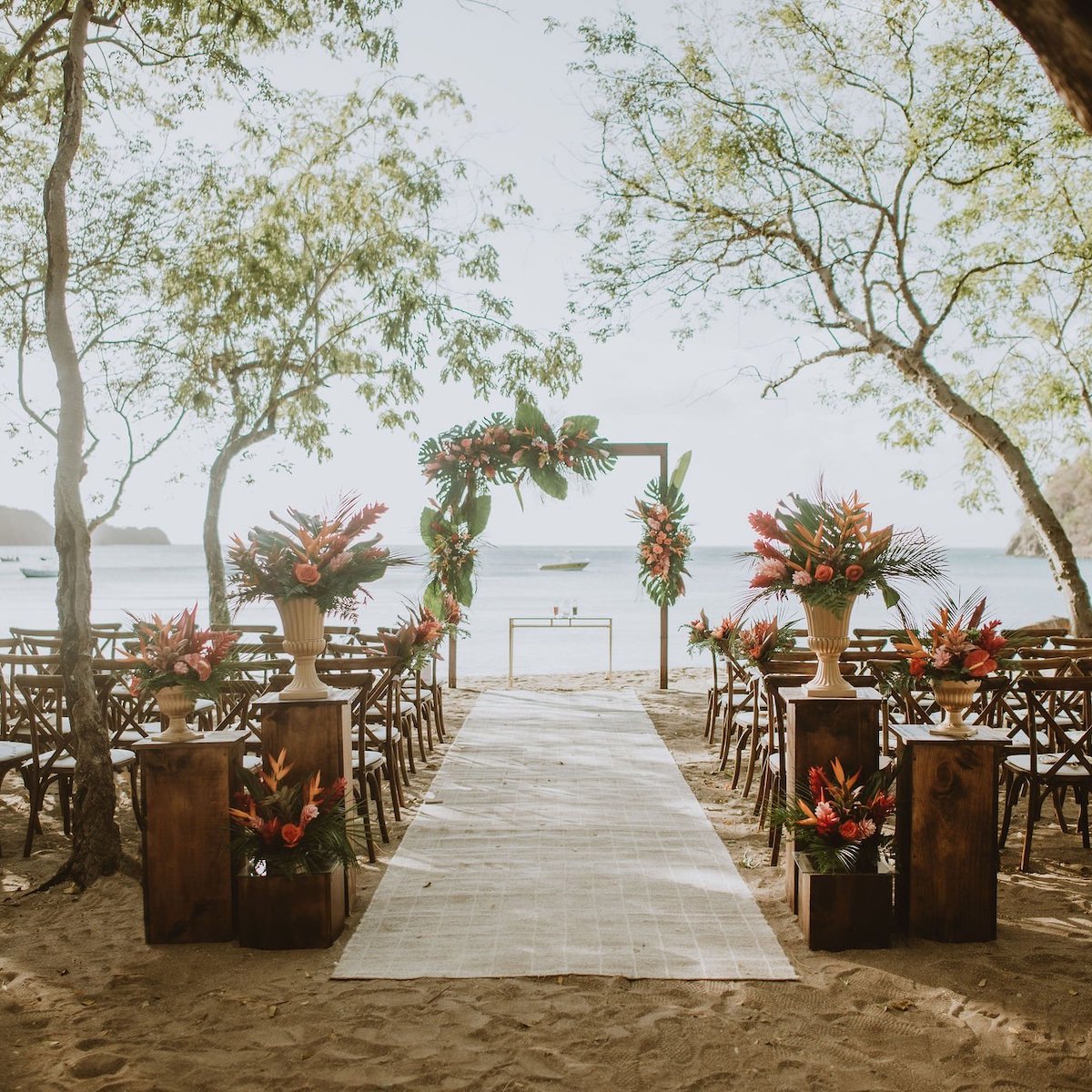 An outdoor wedding setup on a beach in Costa Rica with a decorated archway, floral arrangements, and rows of wooden chairs facing the ocean.
