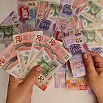 Hands holding Mexican peso banknotes over a background of scattered bills, symbolizing fluctuating currency exchange rates.