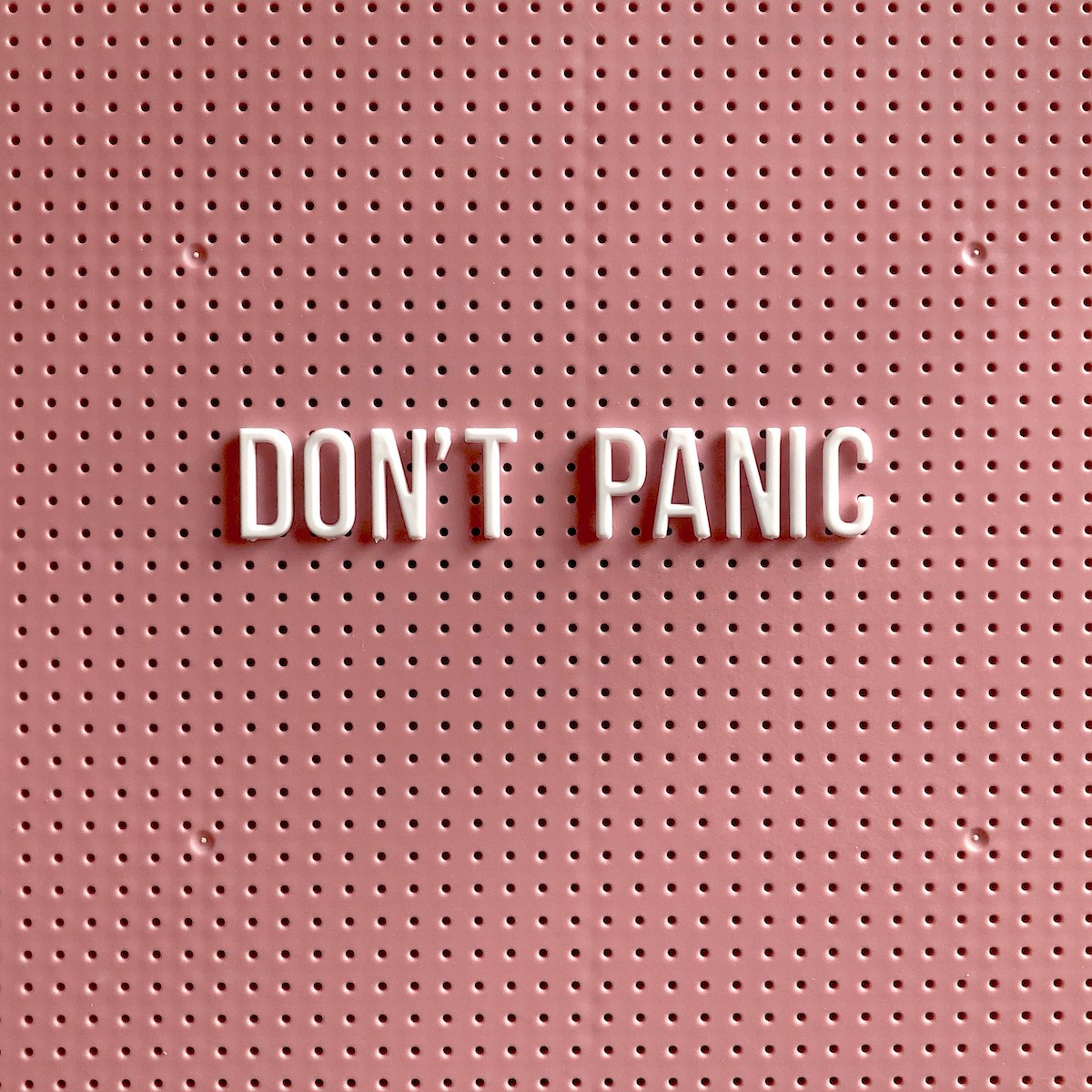 Plastic letters spelling out "don't panic" on a pegboard background, illustrating what not to do the week of your wedding.