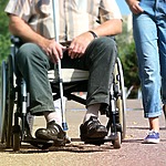 A person in a wheelchair holds a cane resting on their lap while another person stands nearby. The scene portrays the inclusivity often found at handicap accessible wedding venues, set beautifully outdoors.