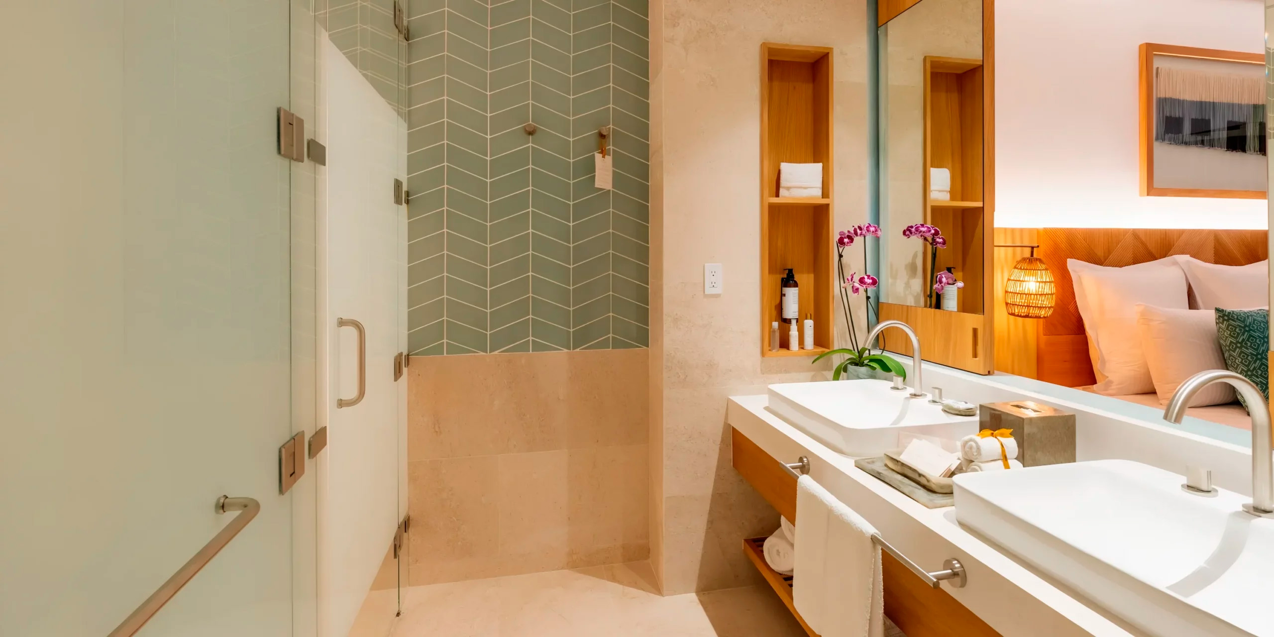 The bathroom at Dreams Estrella del Mar is elegantly designed for a destination wedding retreat, featuring a glass shower, twin sinks, mirrors, and orchid shelves.