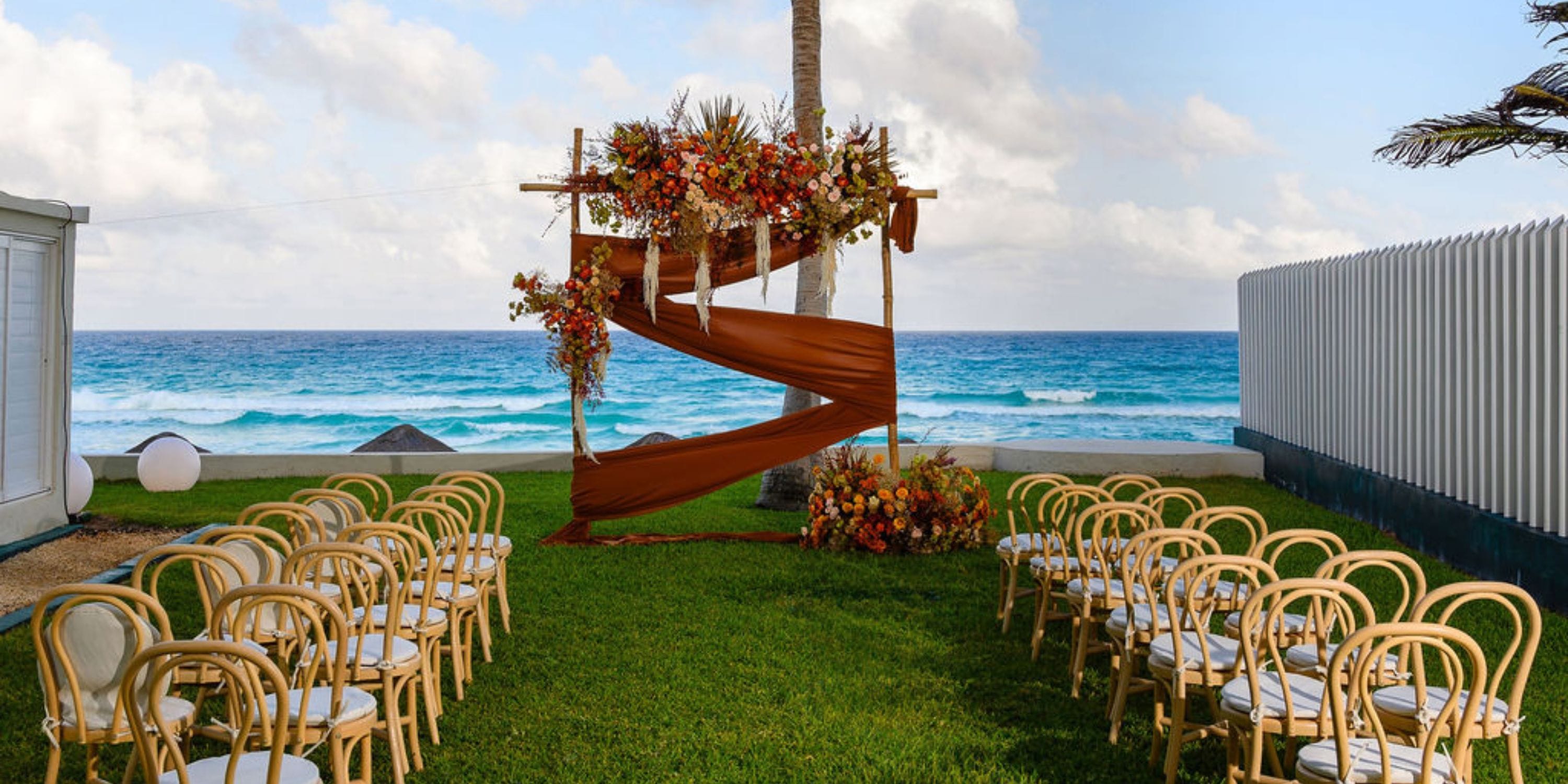 Destination wedding setup at Hilton Cancun Mar Caribe with chairs facing a floral arch by the ocean.