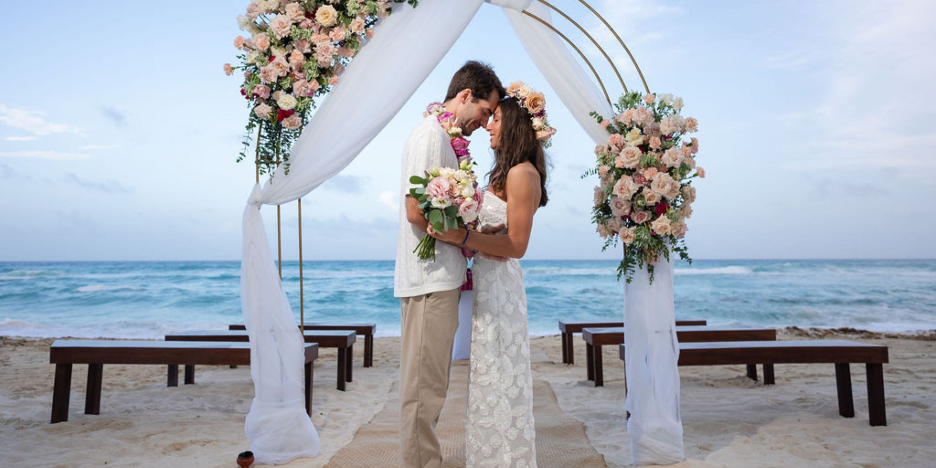 A couple stands beneath a floral arch on the beach at Hilton Cancun Mar Caribe during a destination wedding.