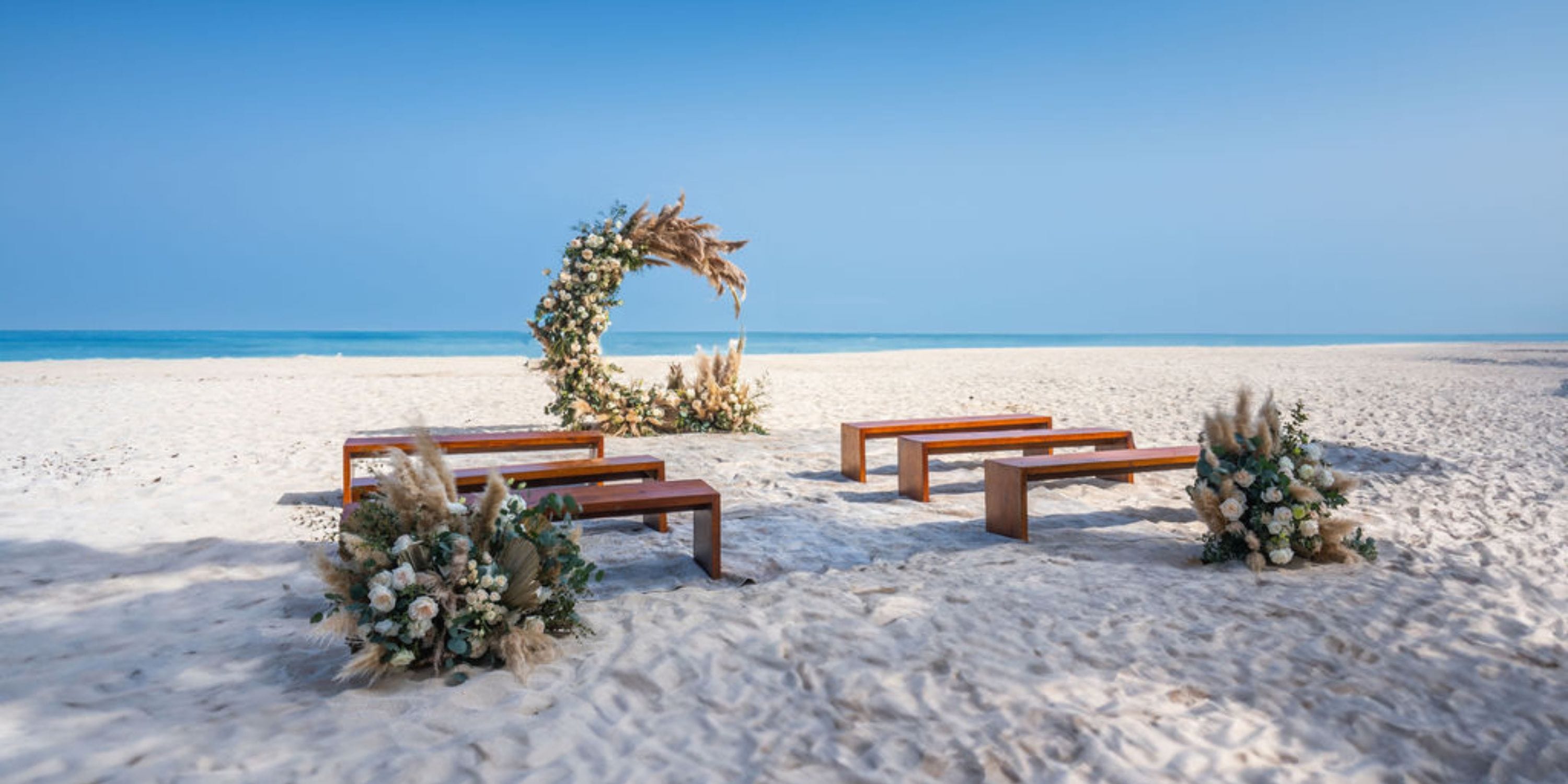 Destination wedding setup on the beach at Hilton Cancun Mar Caribe, featuring wooden benches and a floral arch.