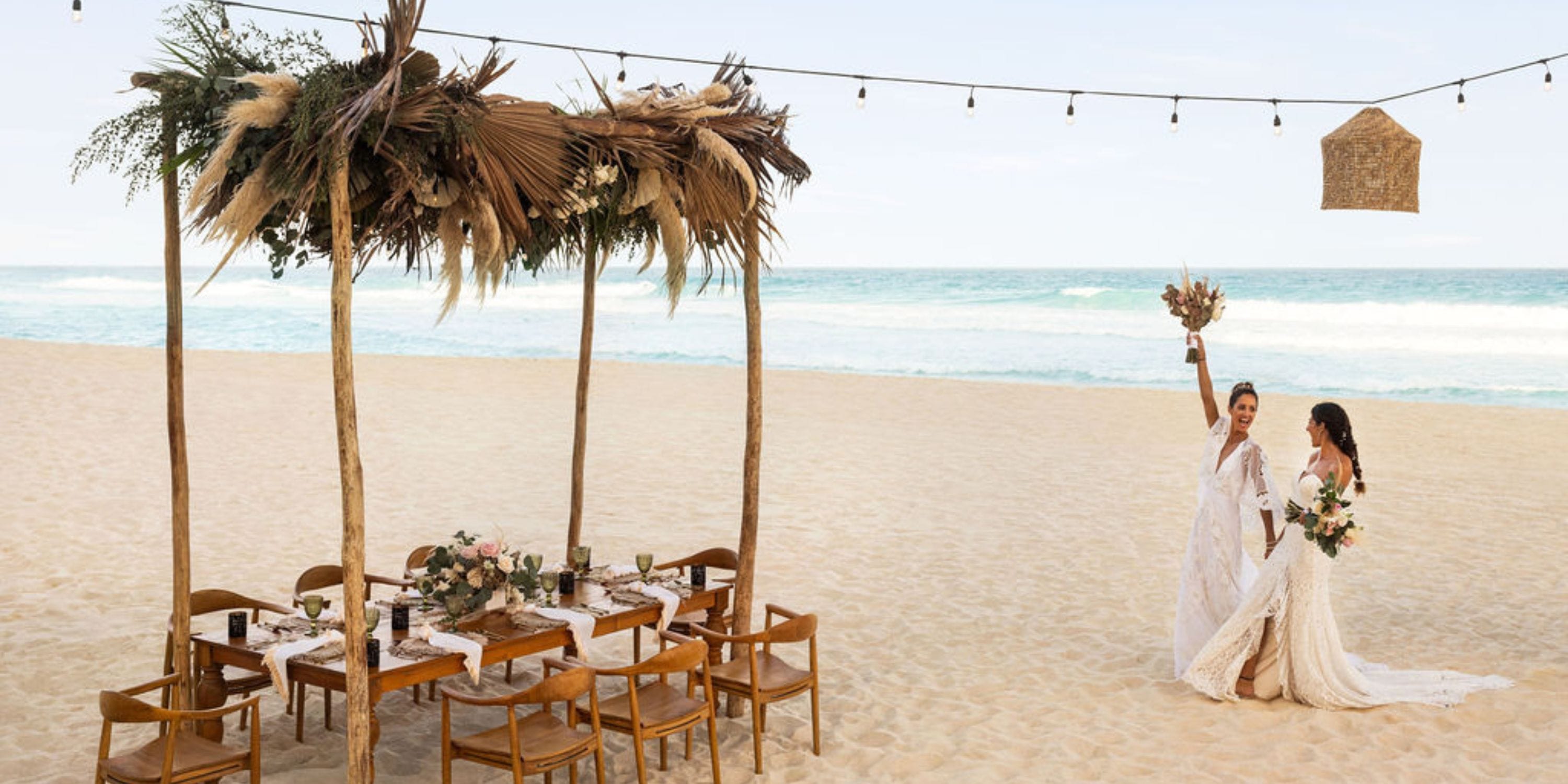 Two brides in wedding dresses stand together on the sandy shore during a destination wedding at Hilton Cancun Mar Caribe.
