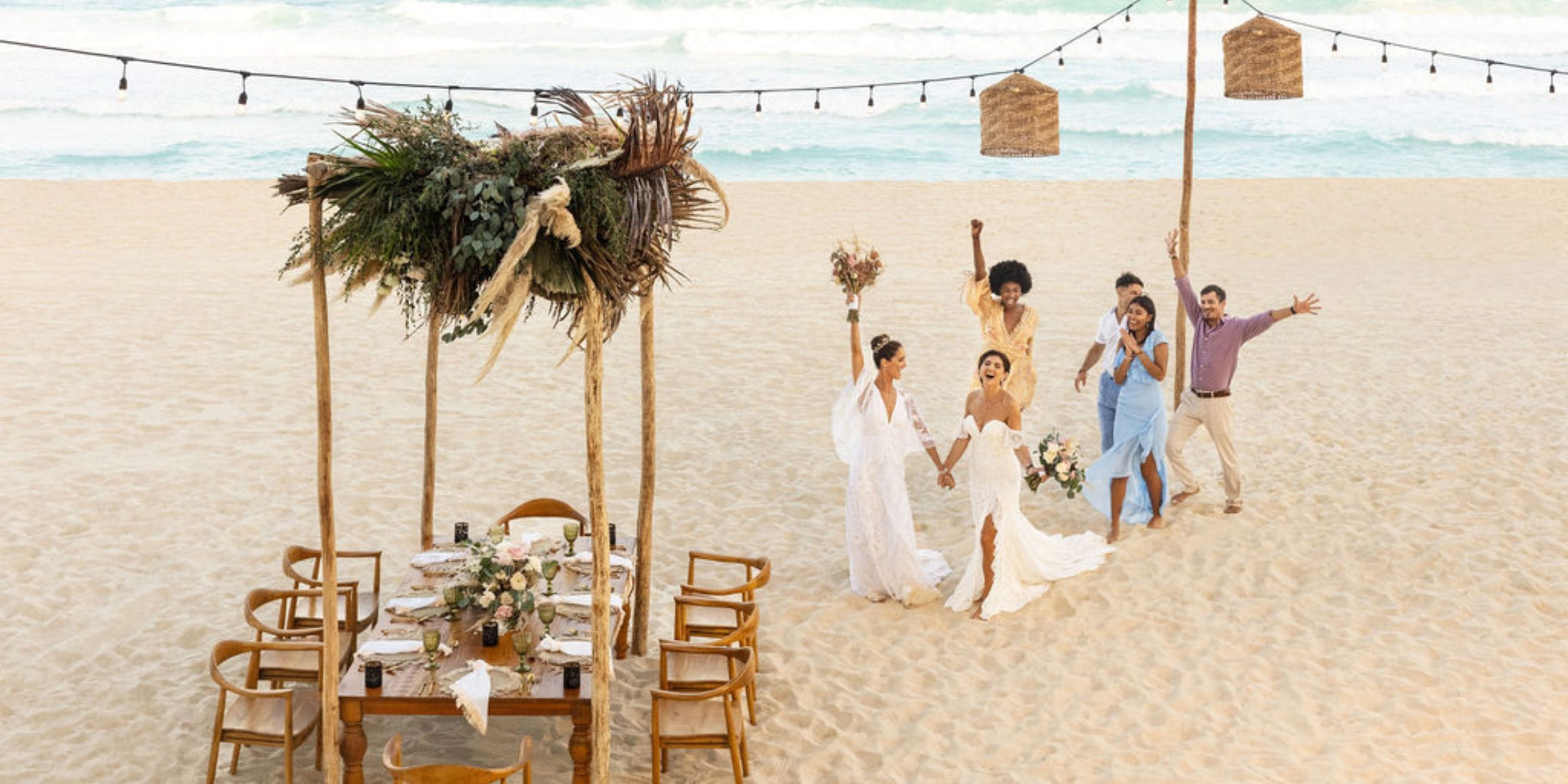 A group enjoys a destination wedding on the sandy beach at Hilton Cancun Mar Caribe by a floral canopy.