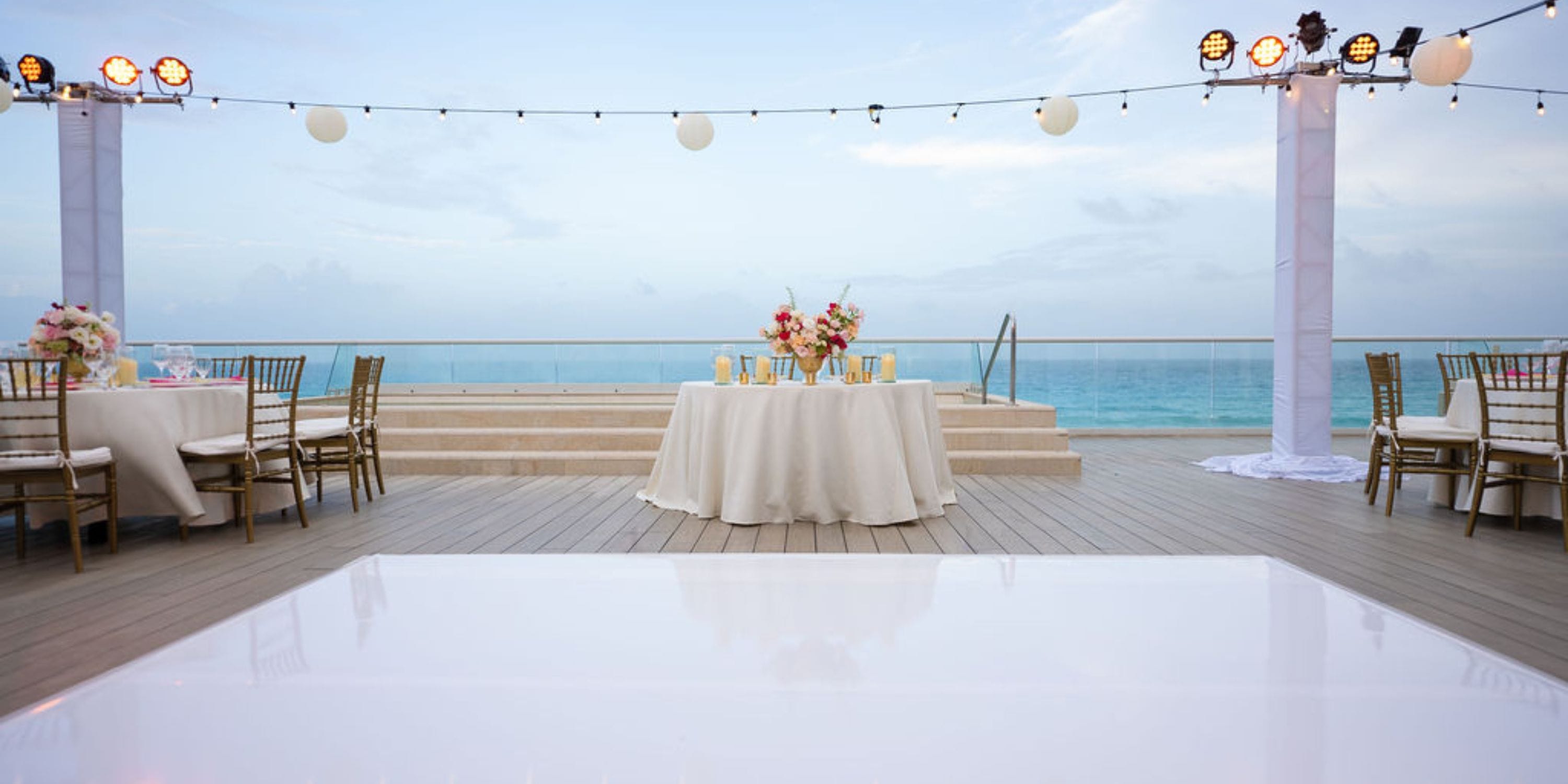 Destination wedding at Hilton Cancun Mar Caribe with round tables and string lights at sunset by the ocean.