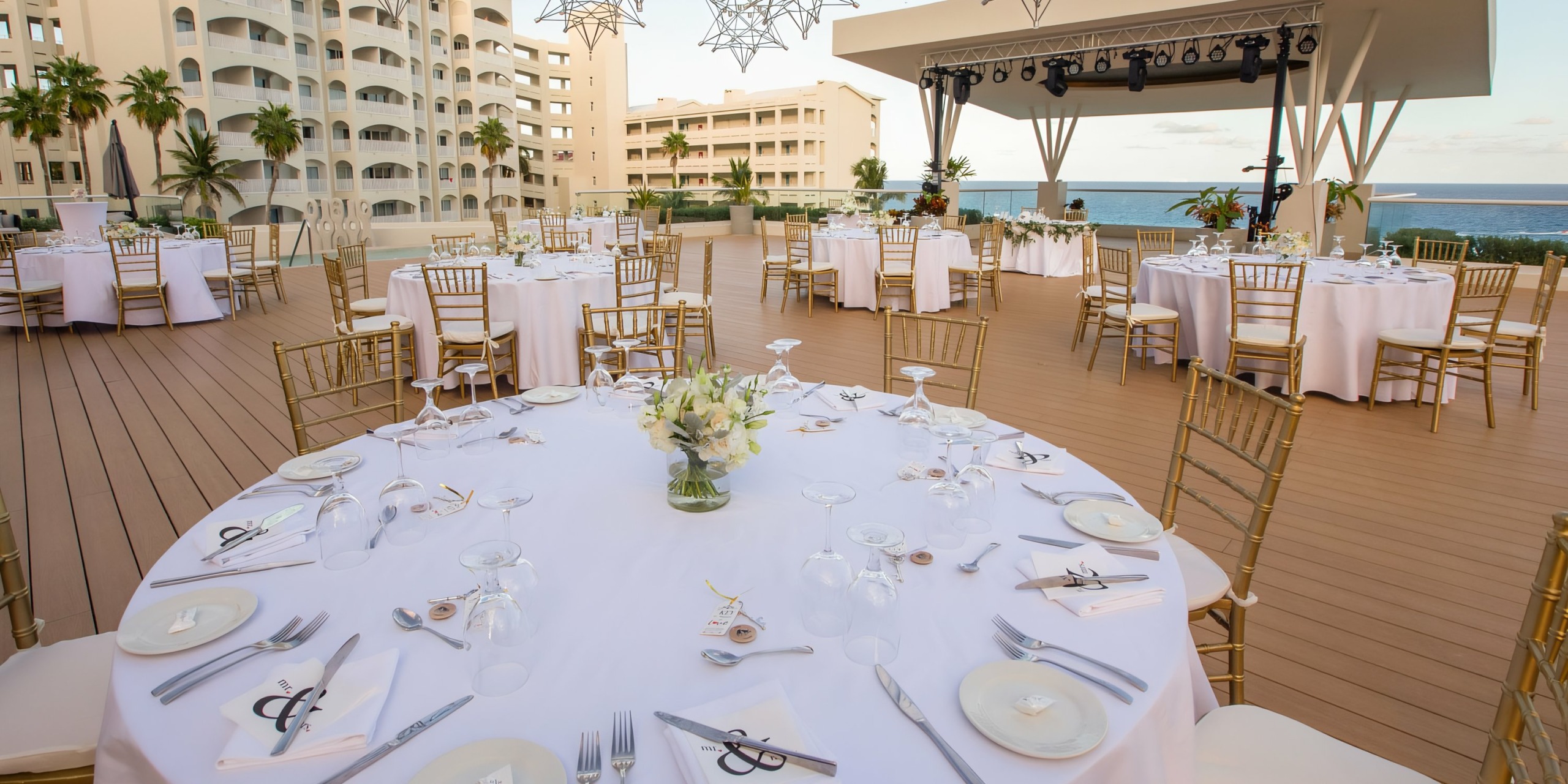 Outdoor banquet setup at Hilton Cancun Mar Caribe, with arranged tables, white chairs, and floral centerpieces overlooking the ocean.