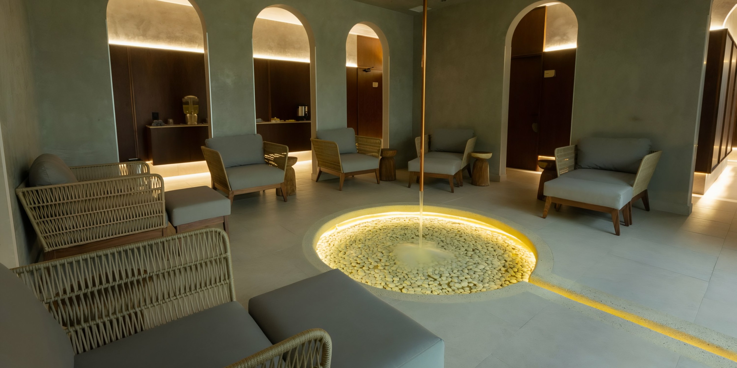 Modern lounge area with neutral tones, featuring a central circular pit with a golden pole, surrounded by armchairs and arched doorways at Hilton Cancun Mar Caribe.