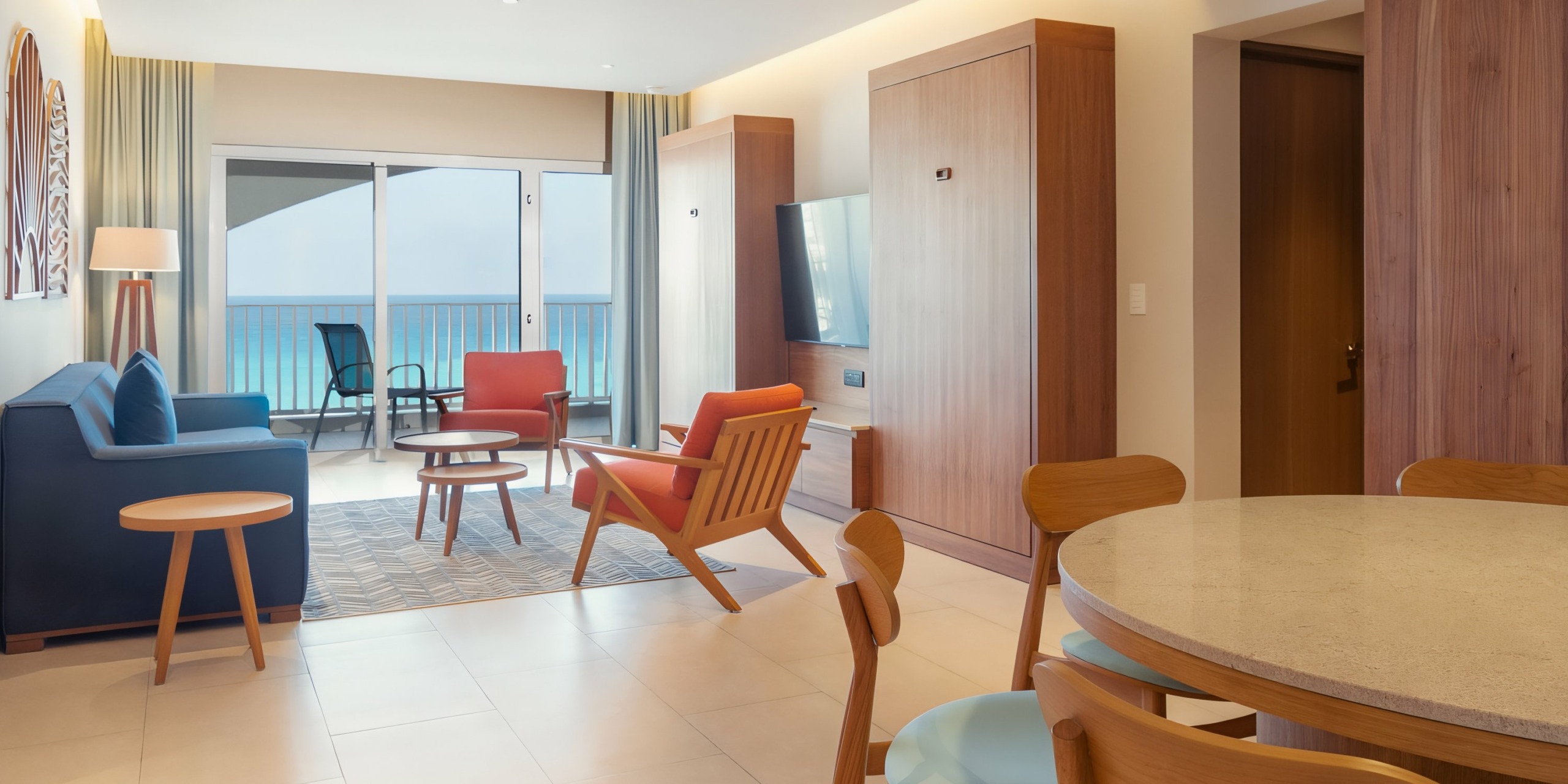 Modern Hilton Cancun Mar Caribe hotel room interior with a seating area, dining table, and an open balcony door showing an ocean view.