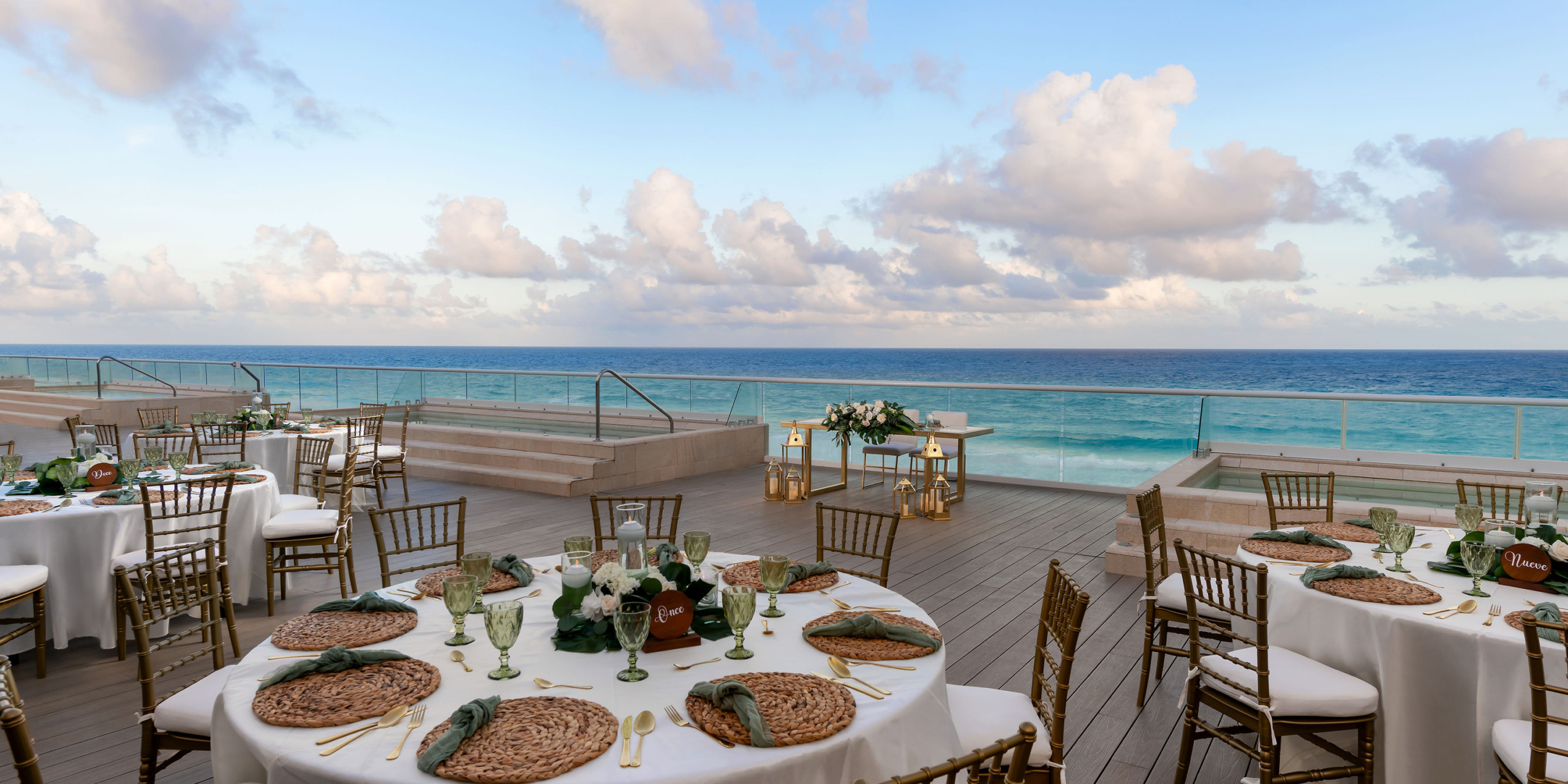 Hilton Cancun Mar Caribe wedding reception setup with elegantly arranged tables on a wooden deck overlooking a calm ocean under a cloudy sky.