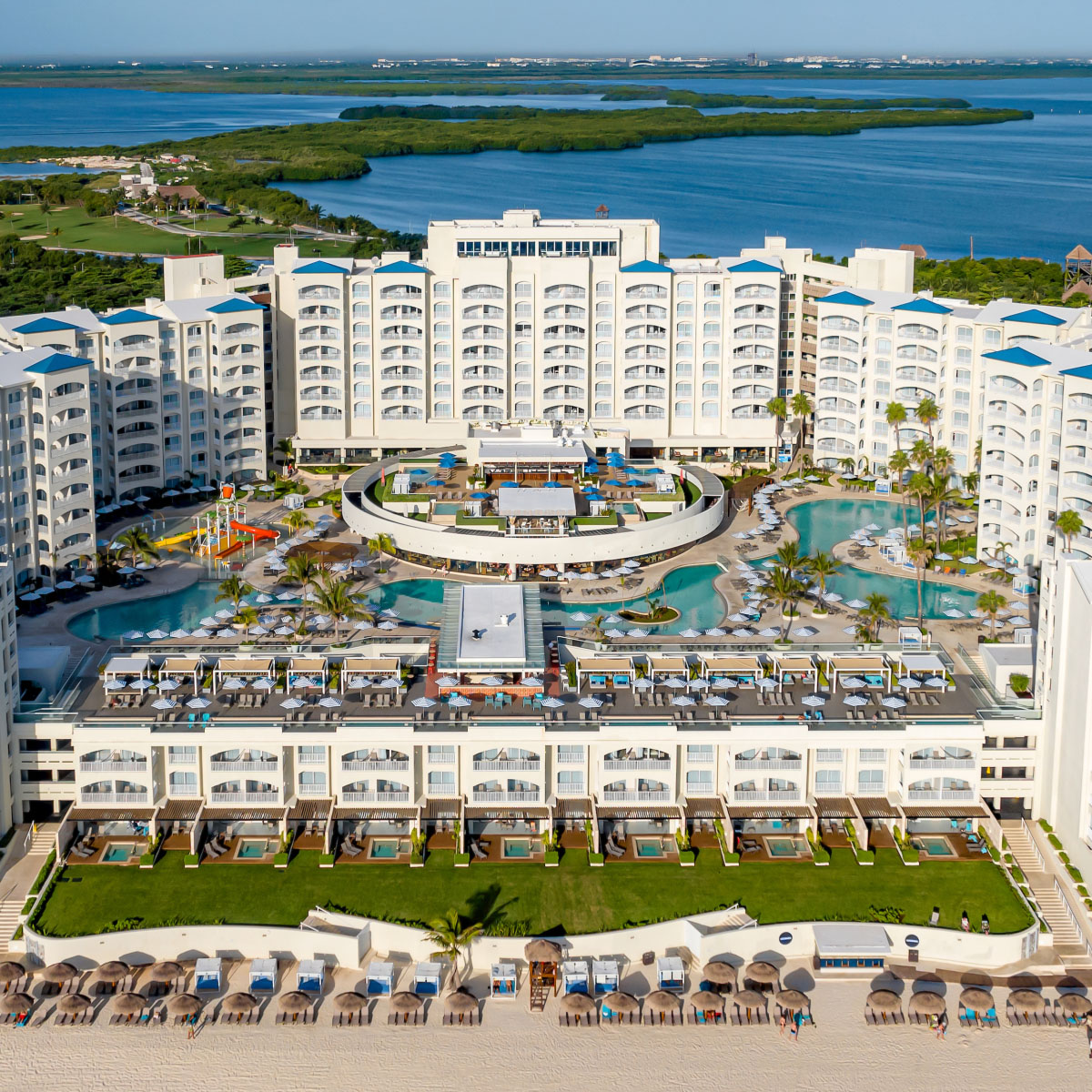 Aerial view of Hilton Cancun Mar Caribe, a large beachfront resort with a curved building surrounding a central pool area, adjacent to a lagoon.