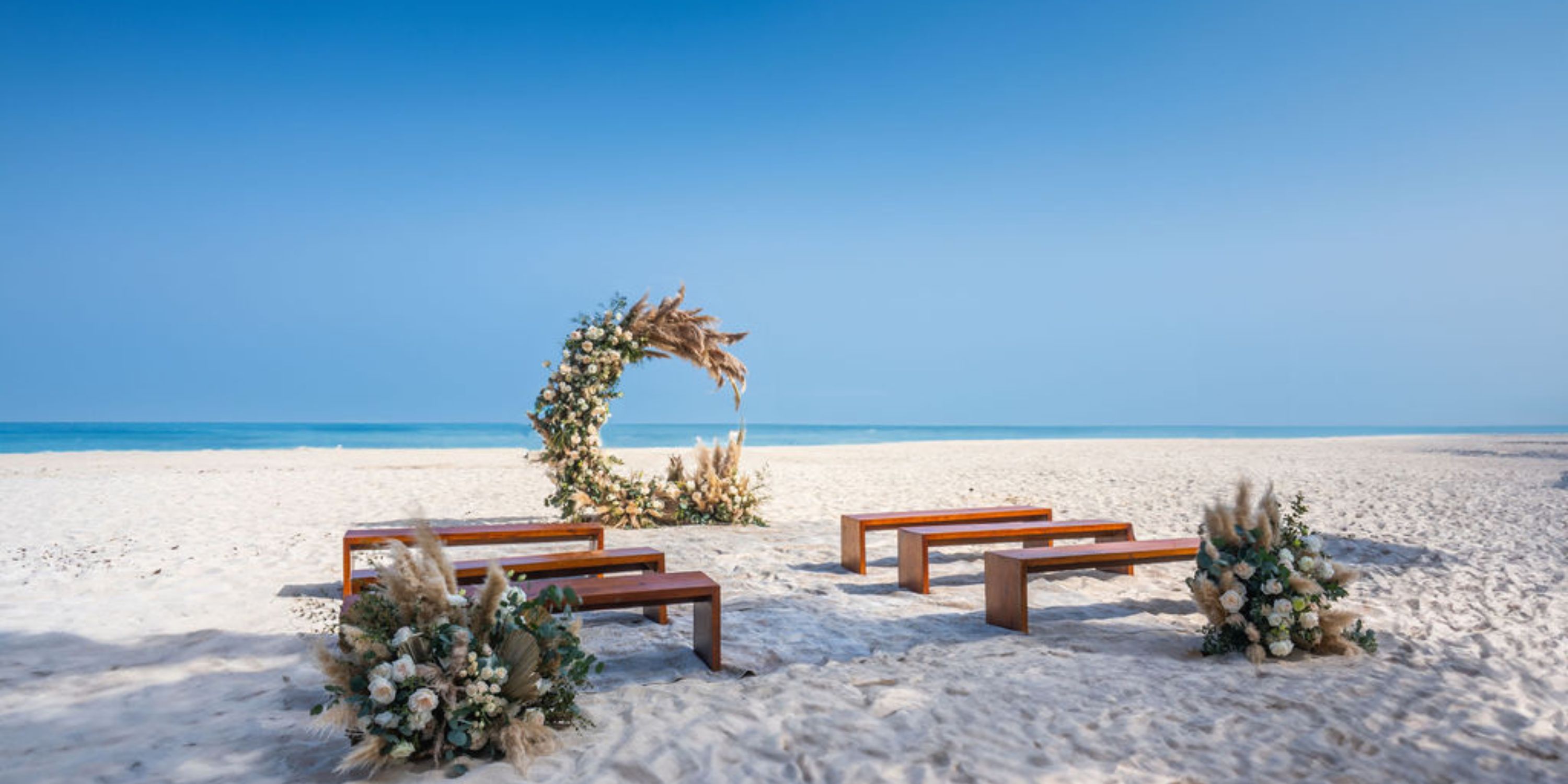 Destination wedding at Hilton Cancun Mar Caribe with wooden benches and floral arch on the sandy beach.