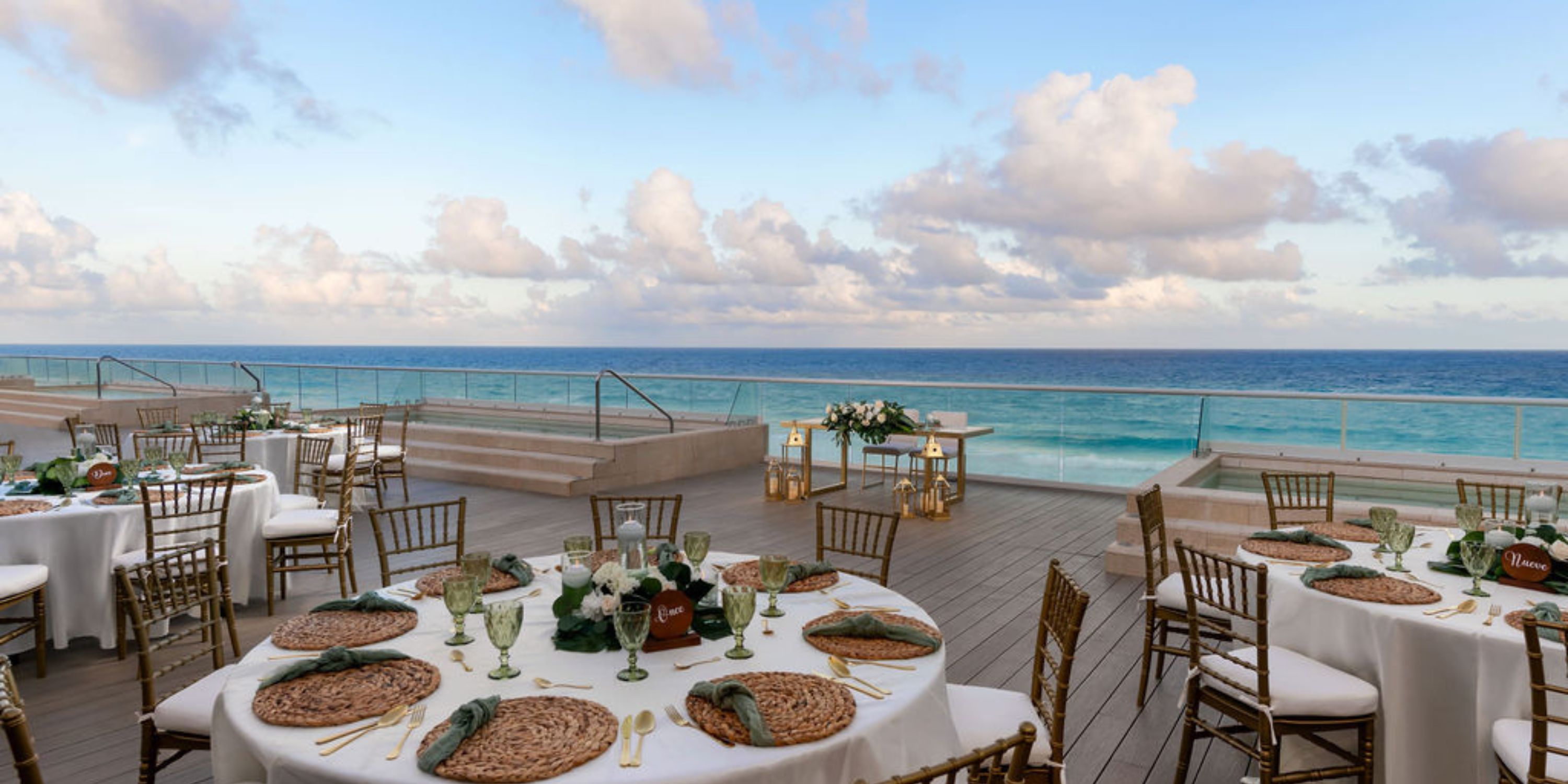 Destination wedding setup at Hilton Cancun Mar Caribe with round tables on a deck at sunset by the ocean.