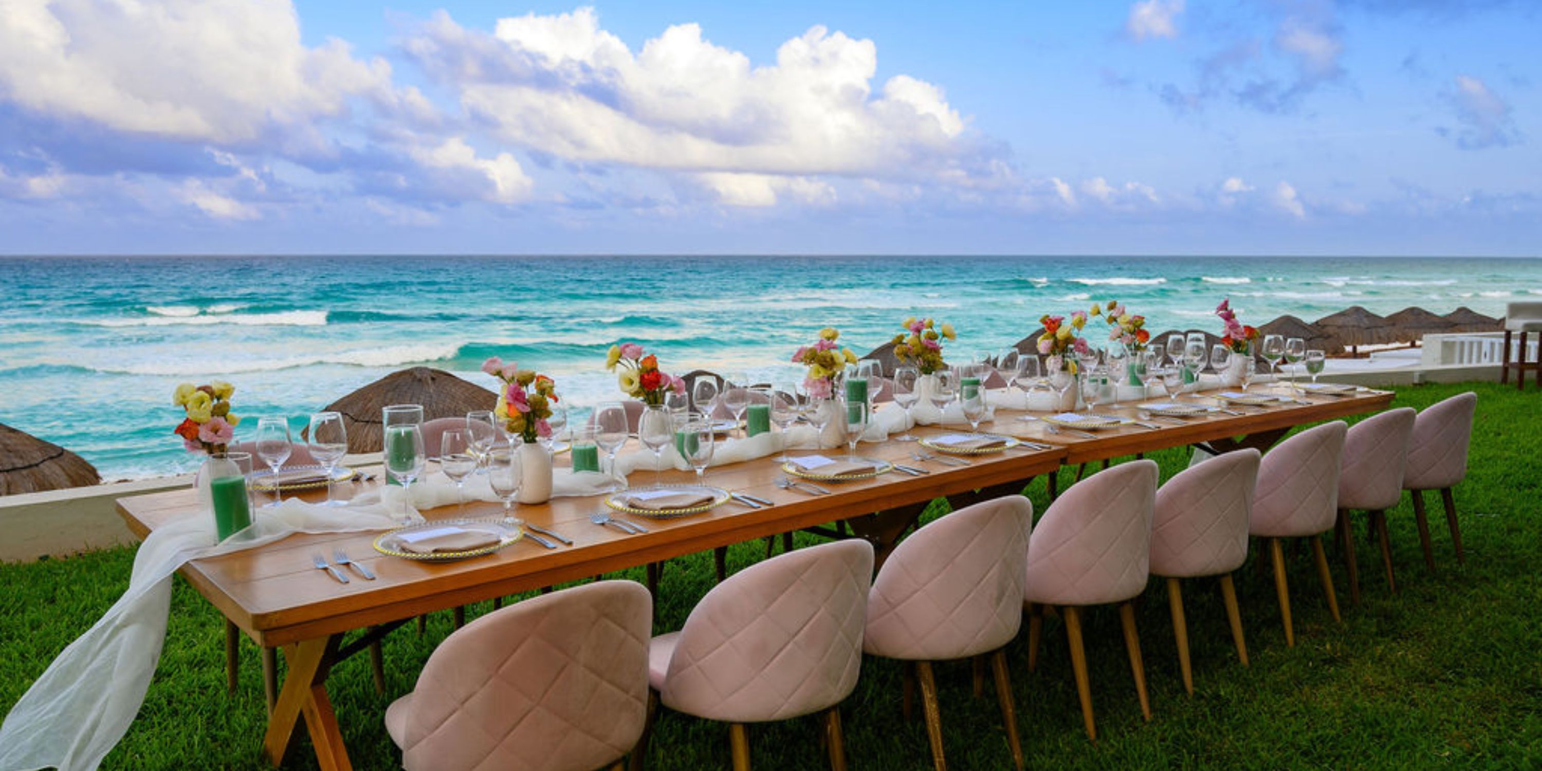 Hilton Cancun Mar Caribe wedding dining table with flowers and plates on grass beside the ocean.