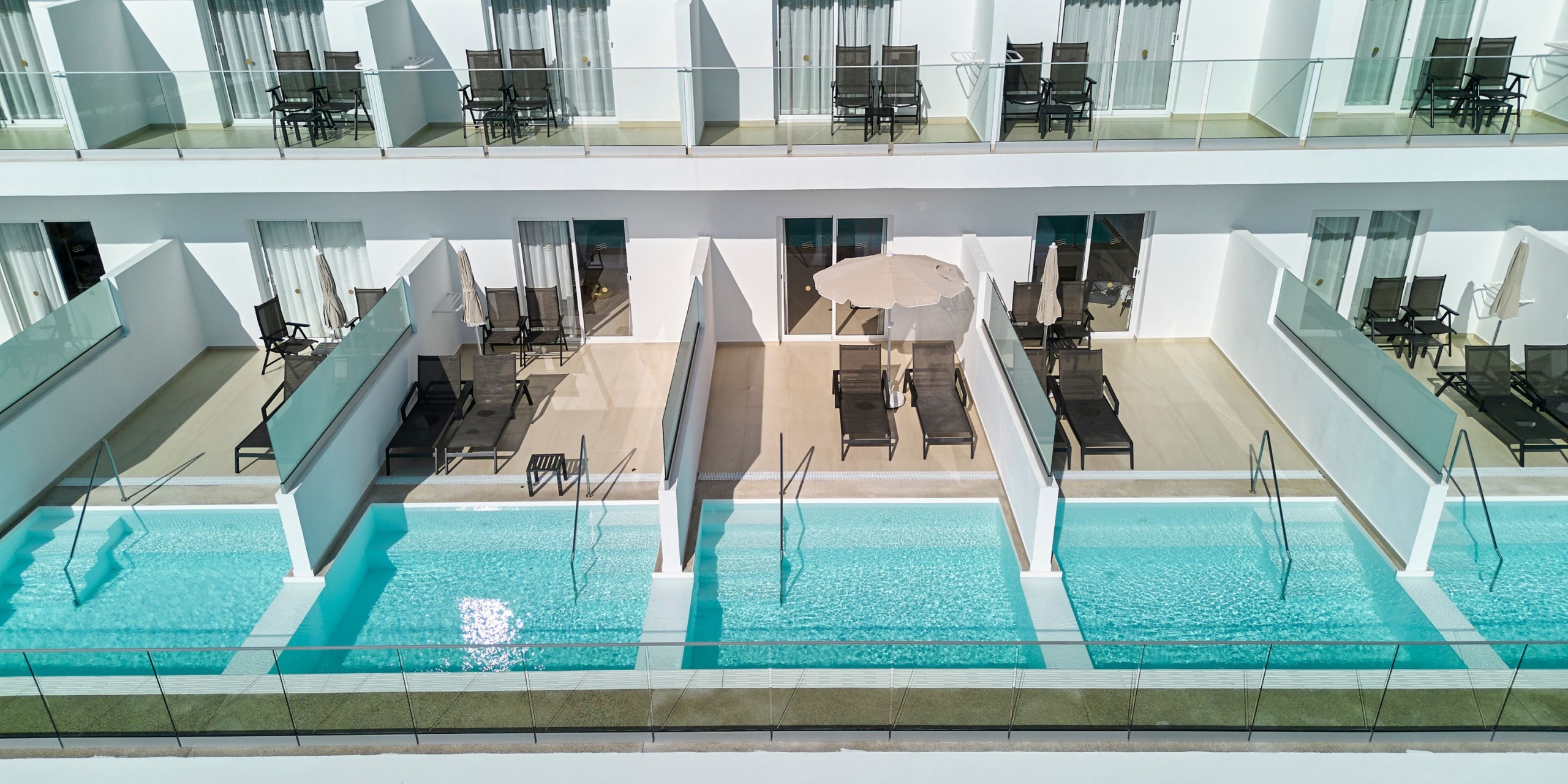 An aerial view of the Hotel RIU Palace Aquarelle reveals modern accommodations with private balconies, each equipped with individual pools and lounge chairs.