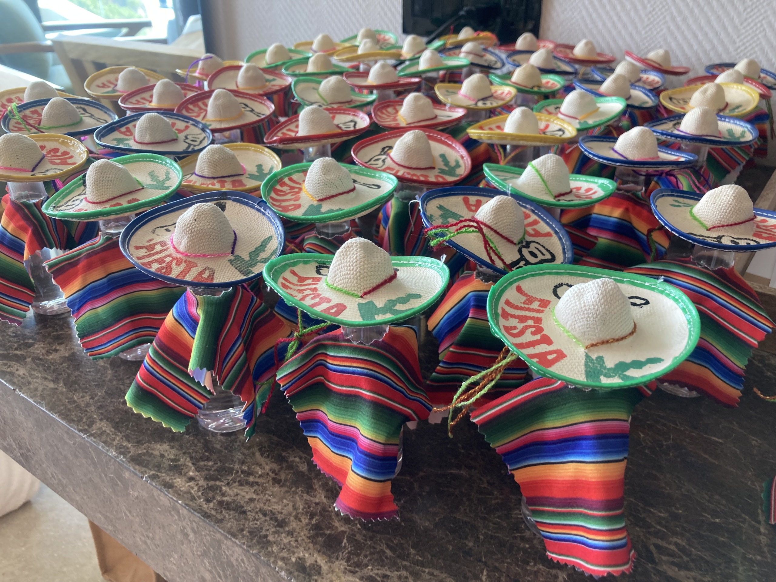 Rows of colorful mini sombreros, each with a vibrant striped fabric and 'Fiesta' written on them, displayed on a table.