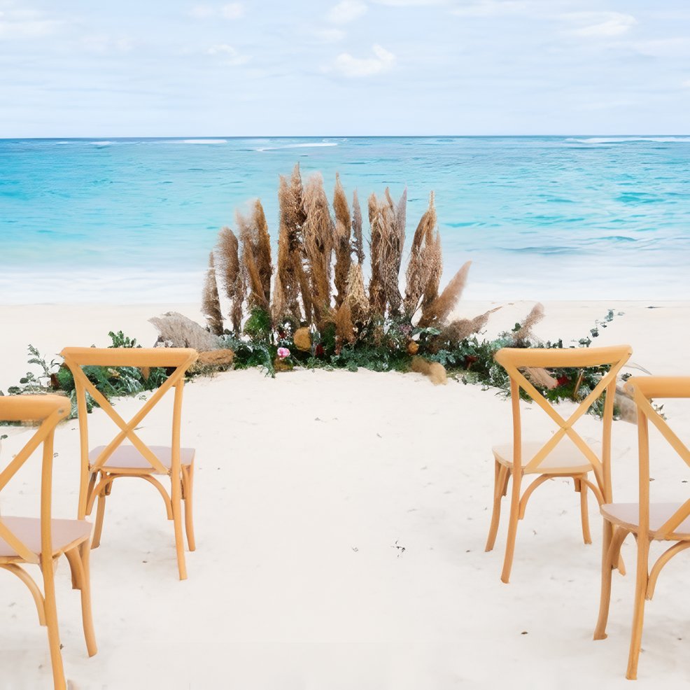 Wooden chairs arranged for a destination wedding on the beach, facing the ocean with pampas grass décor.
