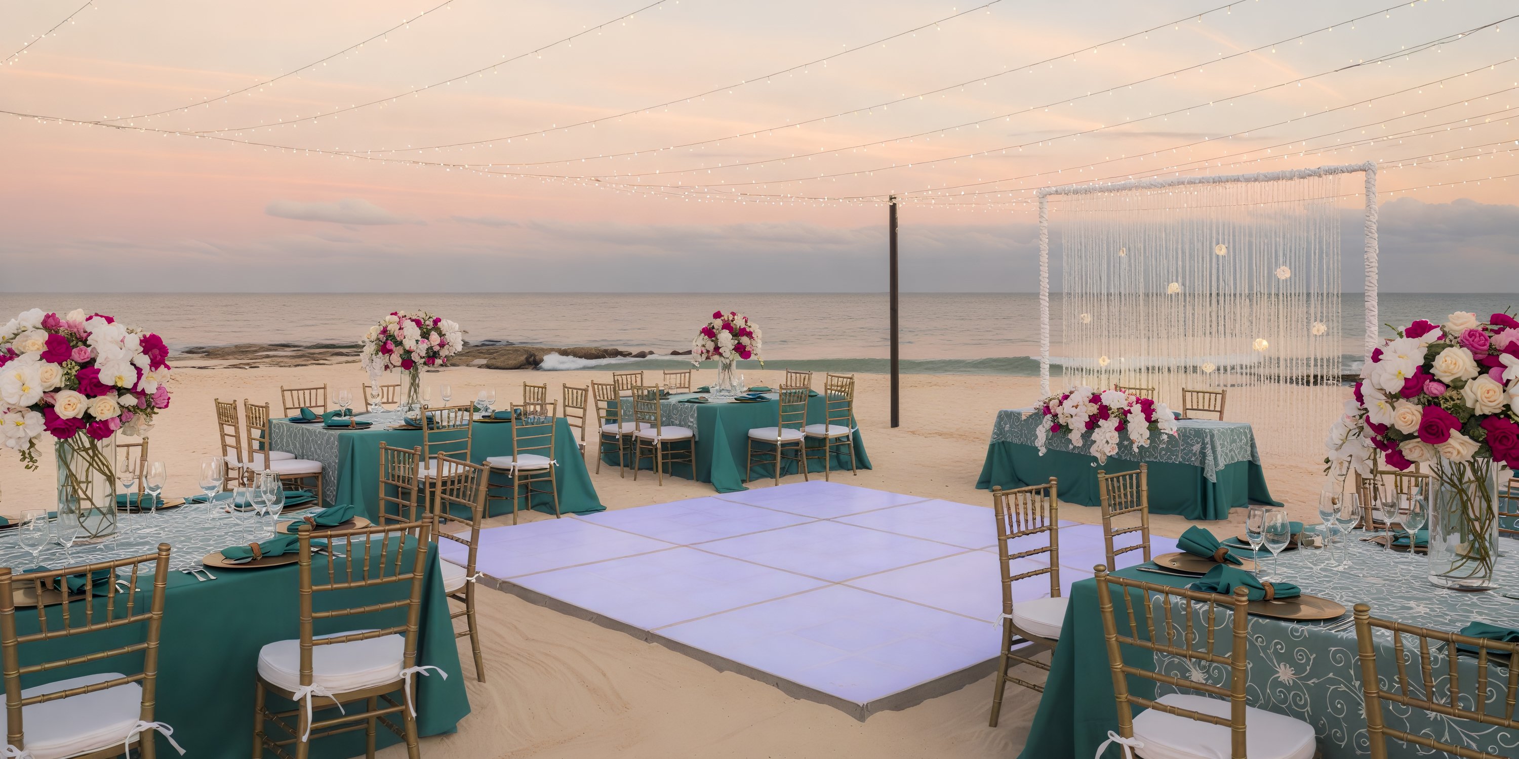 Destination wedding by the beach featuring elegantly arranged tables and chairs, beautiful floral arrangements, and a glowing dance floor illuminated at sunset.