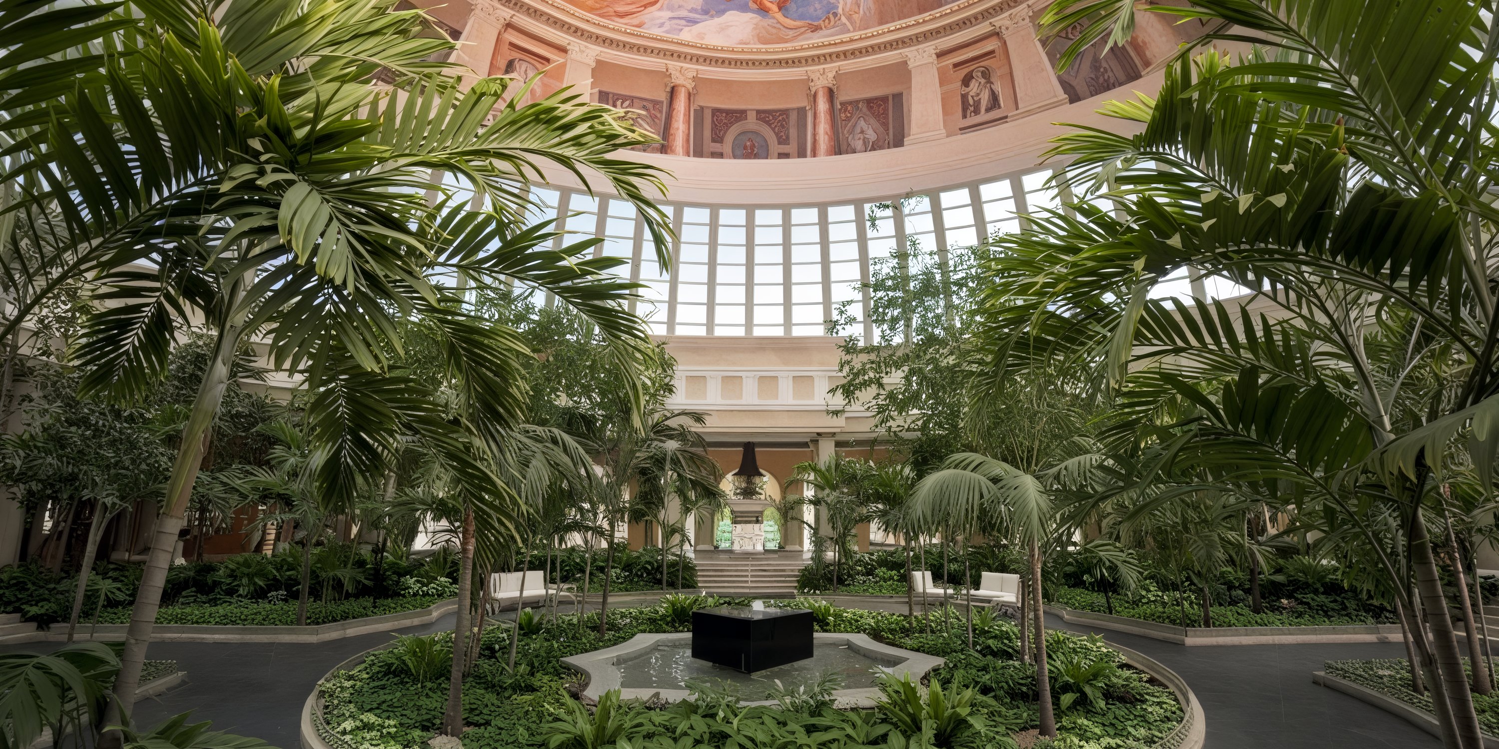 Experience the enchantment of an indoor garden featuring palm trees beneath a vast domed glass ceiling, adorned with breathtaking murals—an idyllic setting for a dream destination wedding.