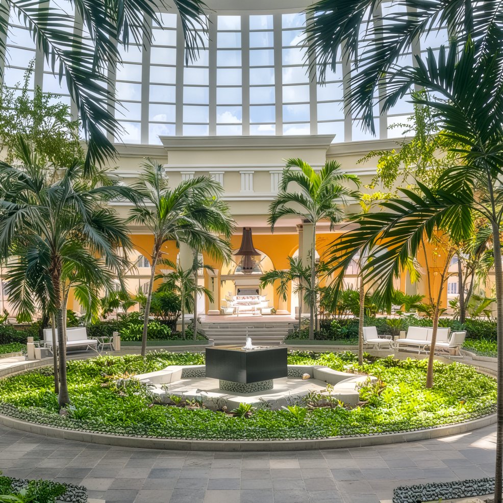 An indoor oasis featuring palm trees, comfortable seating, and a skylight roof – perfect for a destination wedding.