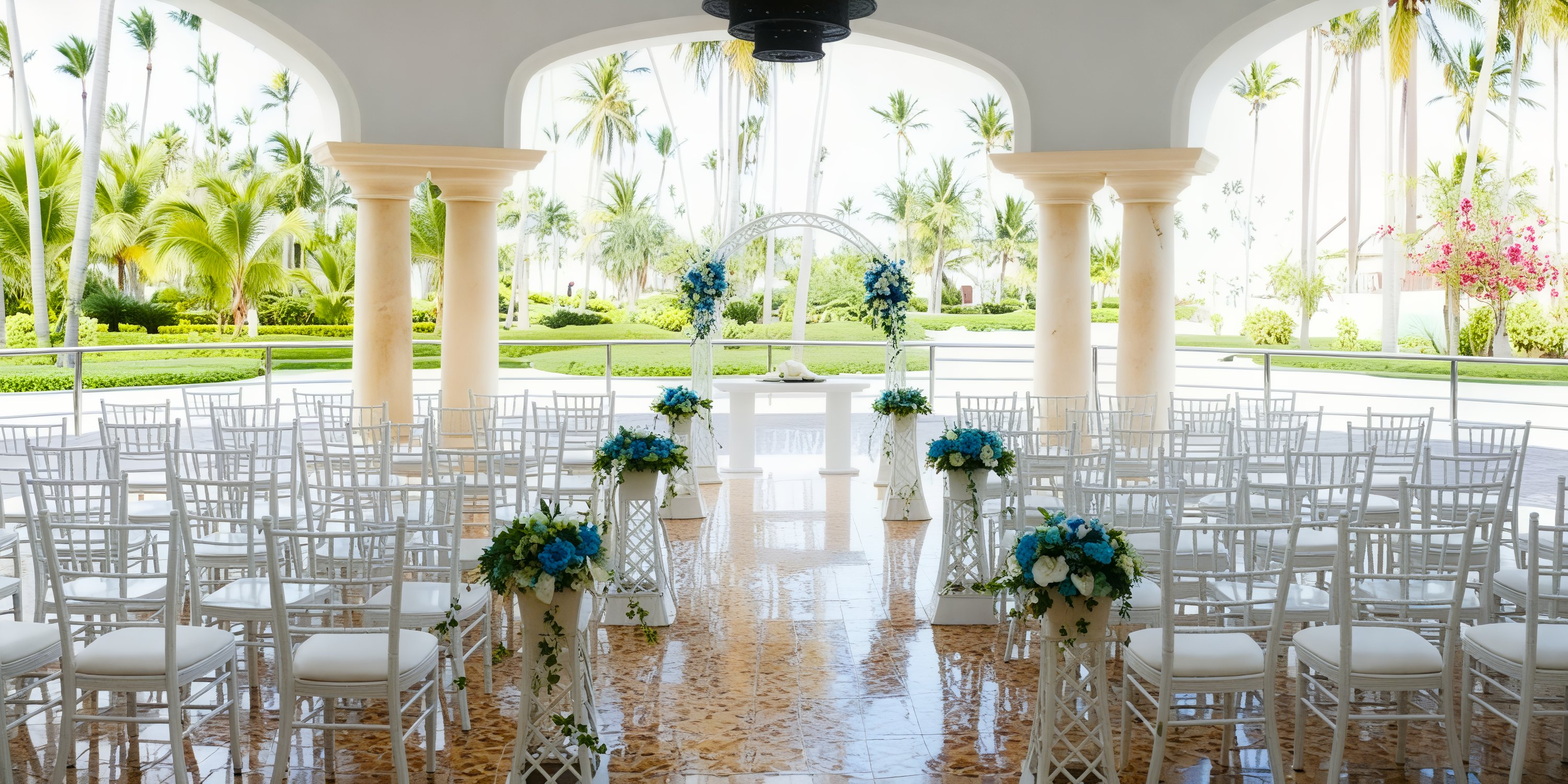 The destination wedding setup at JOIA Bavaro features elegantly arranged white chairs, beautifully complemented by blue floral arrangements and an enchanting archway.