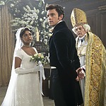A bride in a Penelope Bridgerton wedding dress and groom stand at the altar next to a priest in ornate robes, during a Bridgerton-inspired wedding ceremony in a lavishly decorated venue.