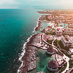 Aerial view of a coastal resort with buildings, pools, and rocky shoreline next to the blue ocean.