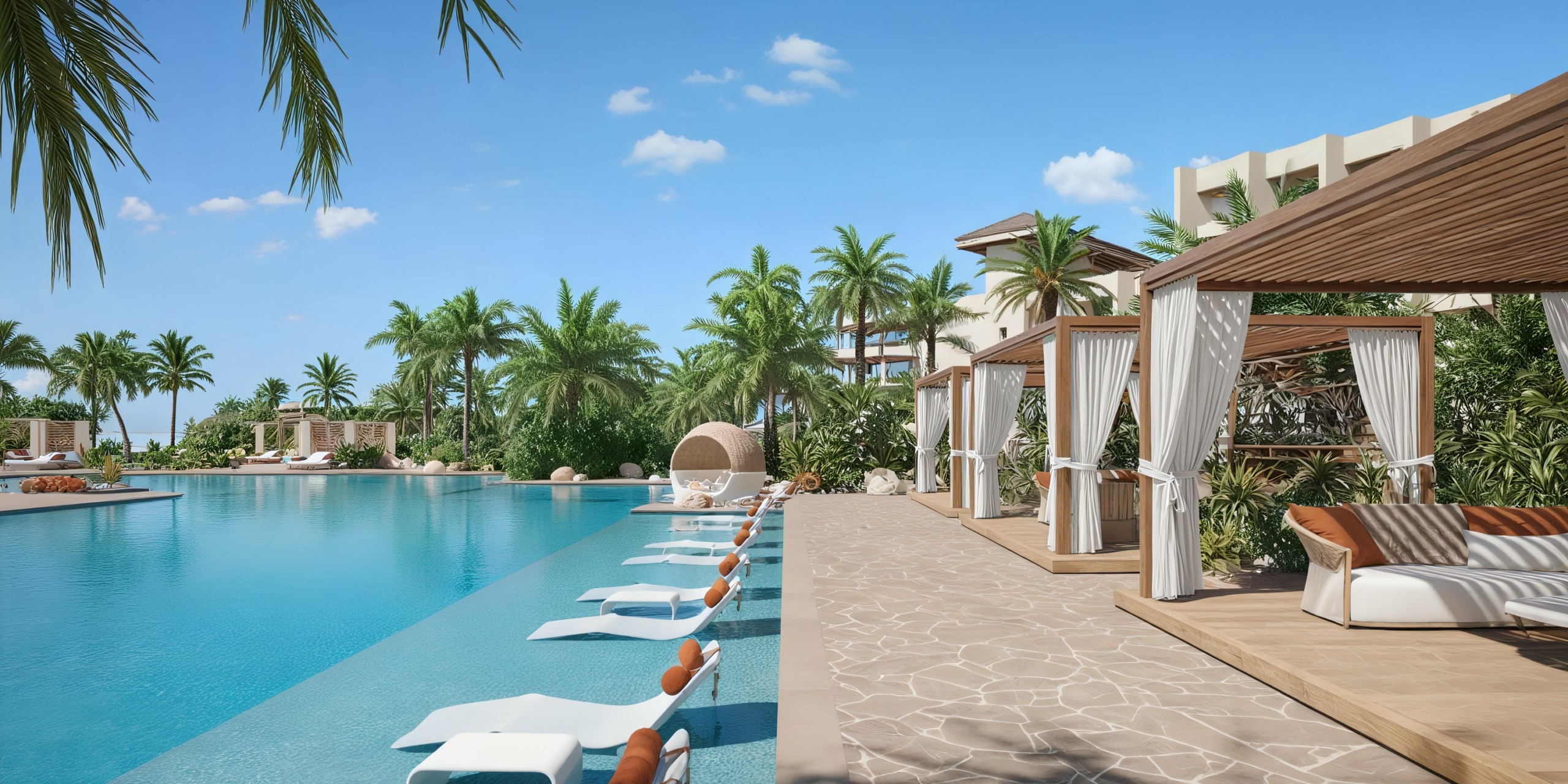 The outdoor pool at JOIA Aruba by Iberostar is surrounded by palm trees, with poolside cabanas and lounge chairs set up under a clear blue sky.