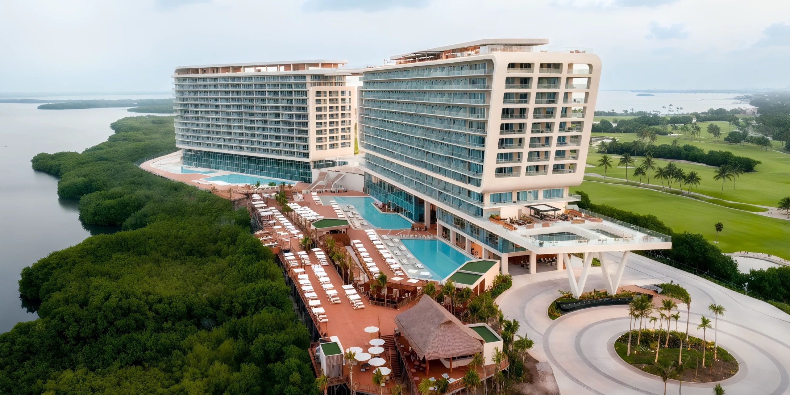 Aerial view of the Hyatt Vivid Grand Island, a modern coastal resort featuring two large buildings, multiple pools, lounge areas, lush greenery, and an adjacent golf course.